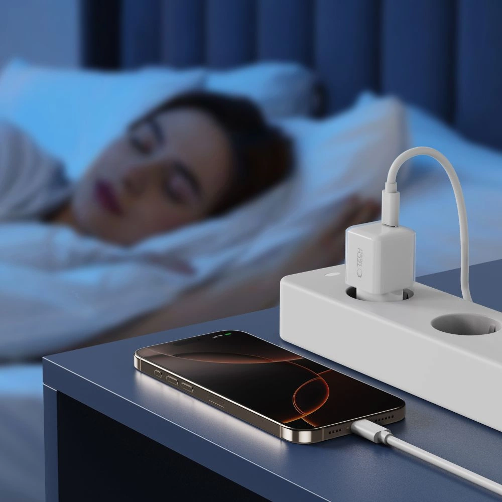 Un smartphone se recharge sur une table de chevet pendant qu'une femme dort.