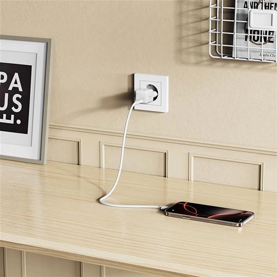 Un smartphone pose sur un bureau en bois est connecte par un cable blanc a un chargeur mural.