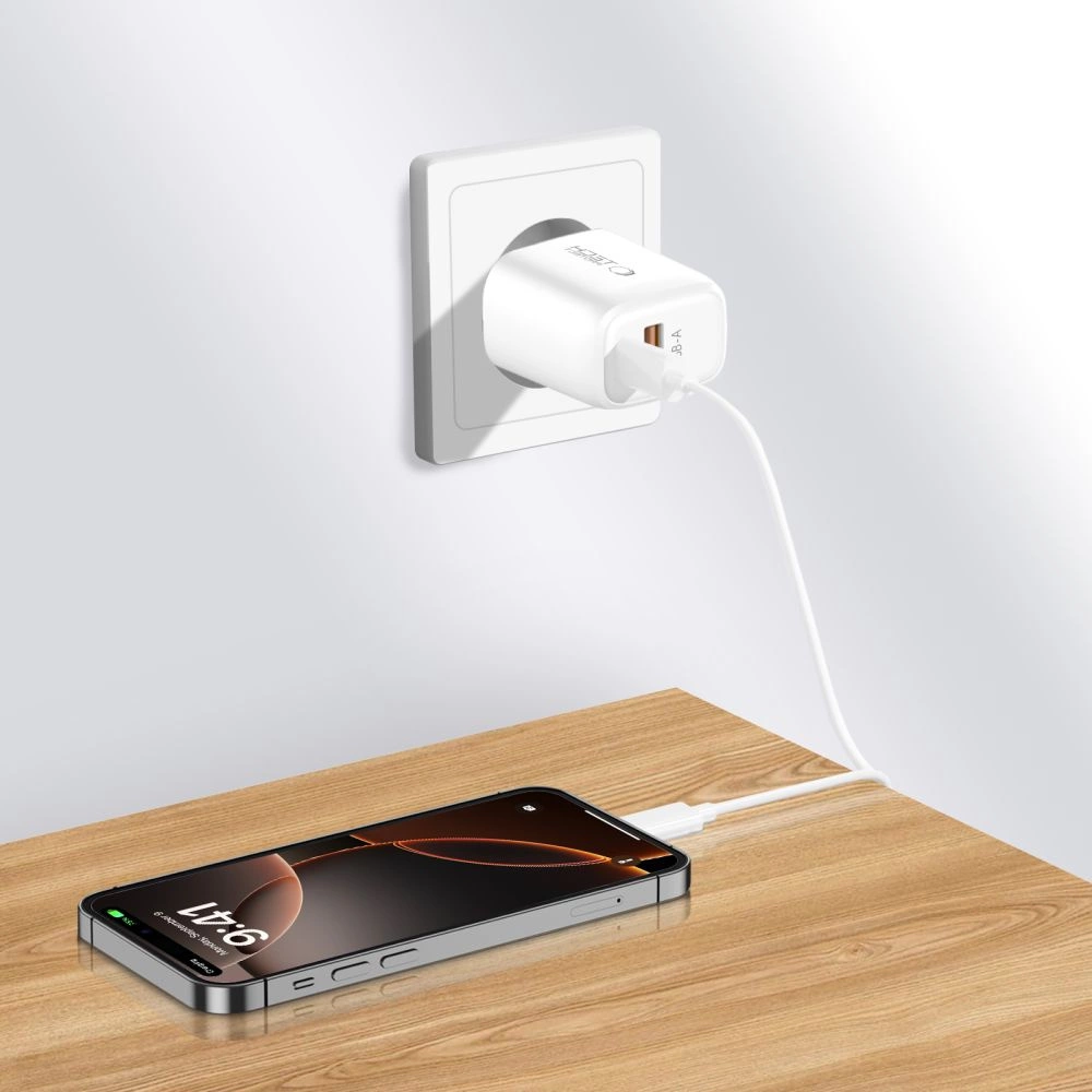 Un chargeur blanc branché au mur recharge un smartphone sur une table en bois.