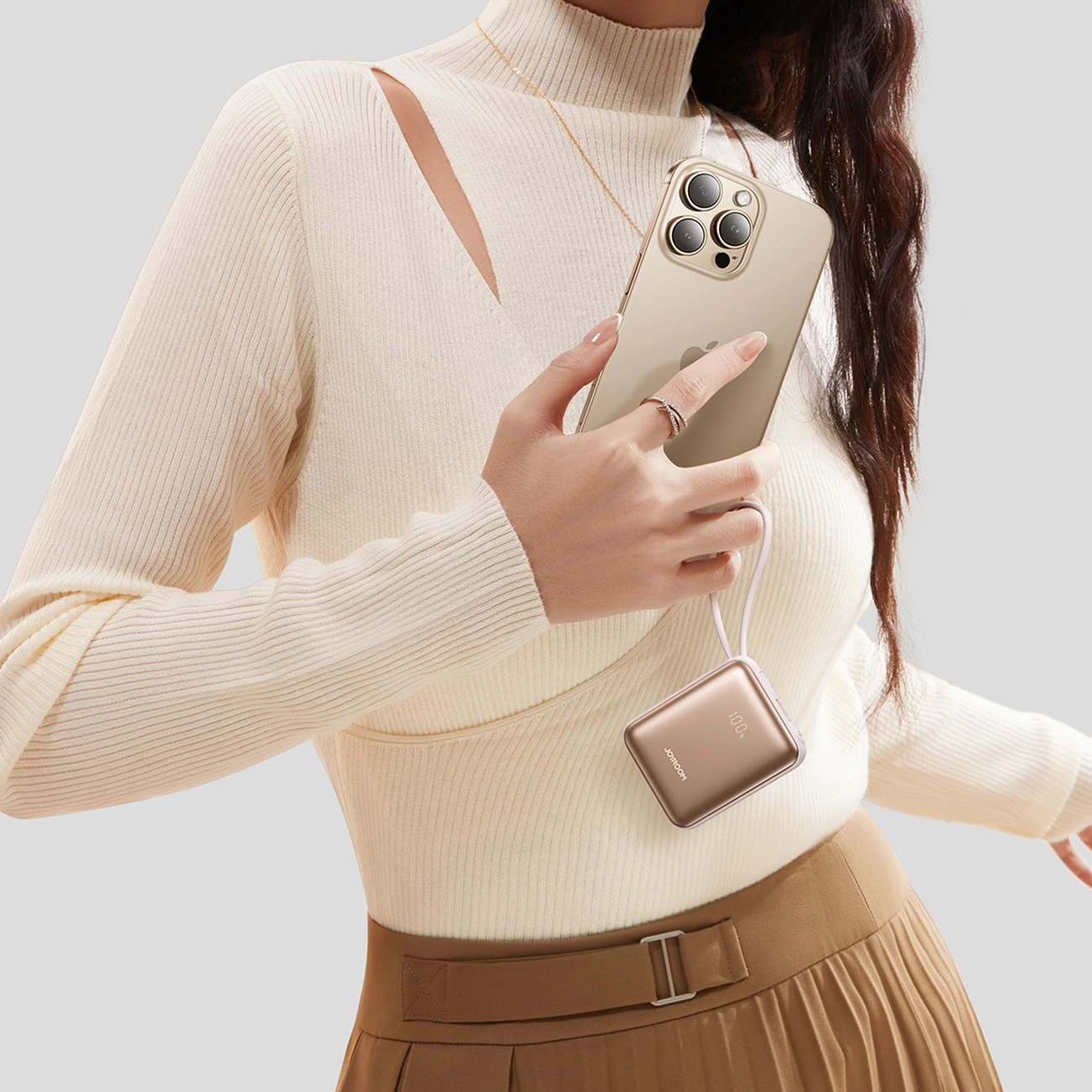 Una donna in top bianco a coste tiene uno smartphone dorato con power bank abbinato.