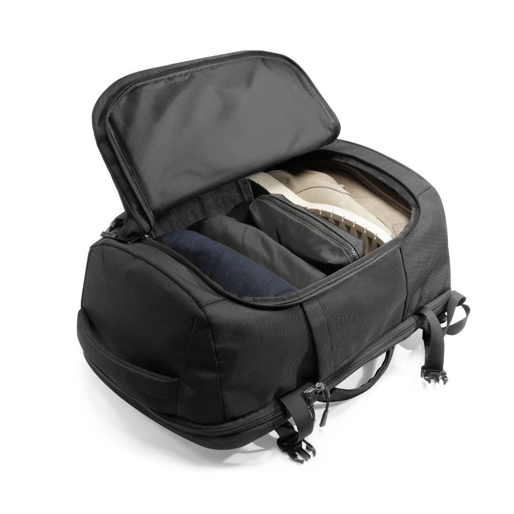 Una borsa da viaggio nera aperta su sfondo bianco mostra vestiti e scarpe ordinati nello scomparto principale.