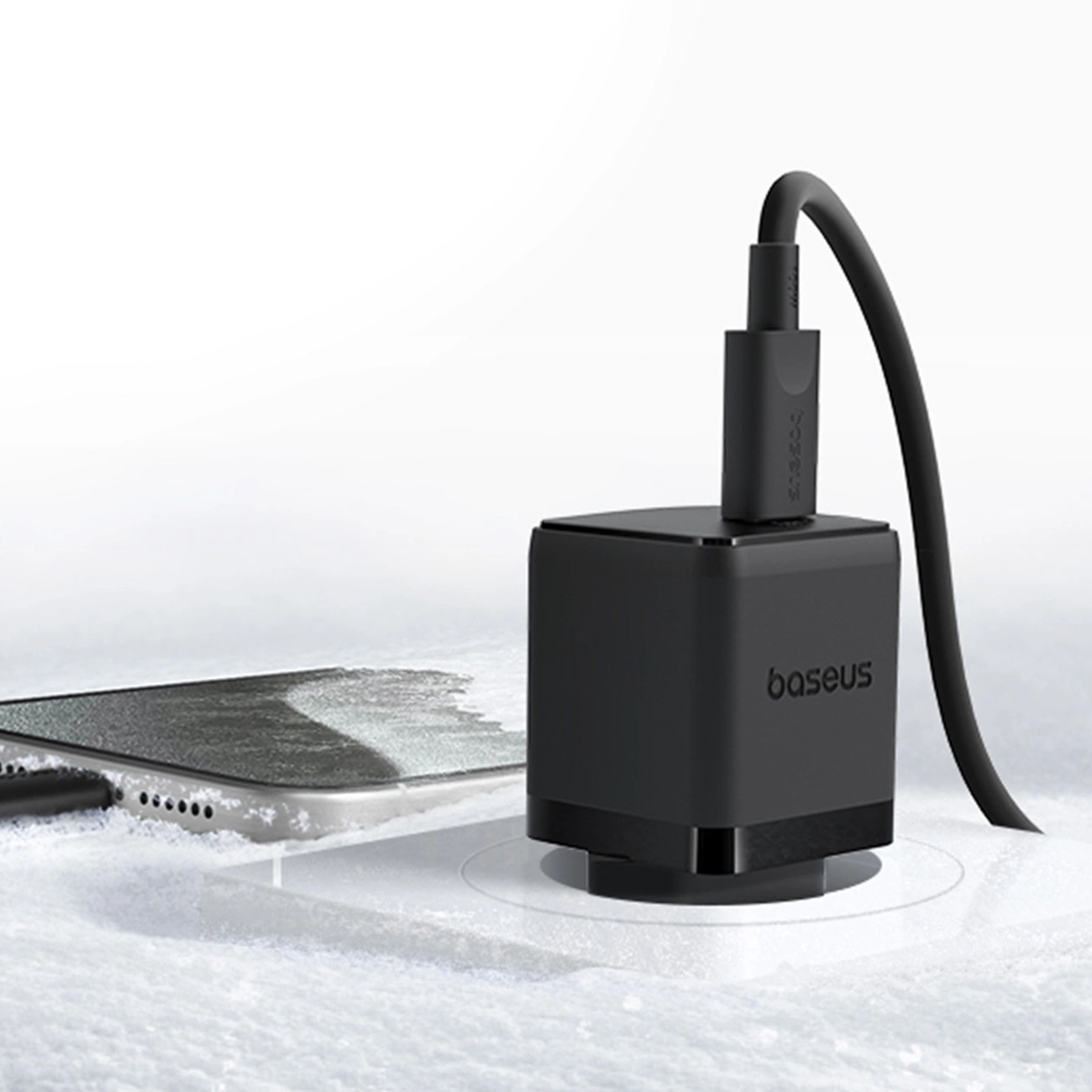 Un chargeur noir Baseus est branché sur une surface enneigée à côté d'un smartphone.
