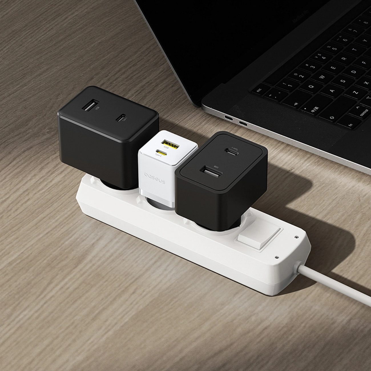 Une multiprise blanche avec trois chargeurs USB branchés se trouve à côté d'un ordinateur portable sur une table en bois.