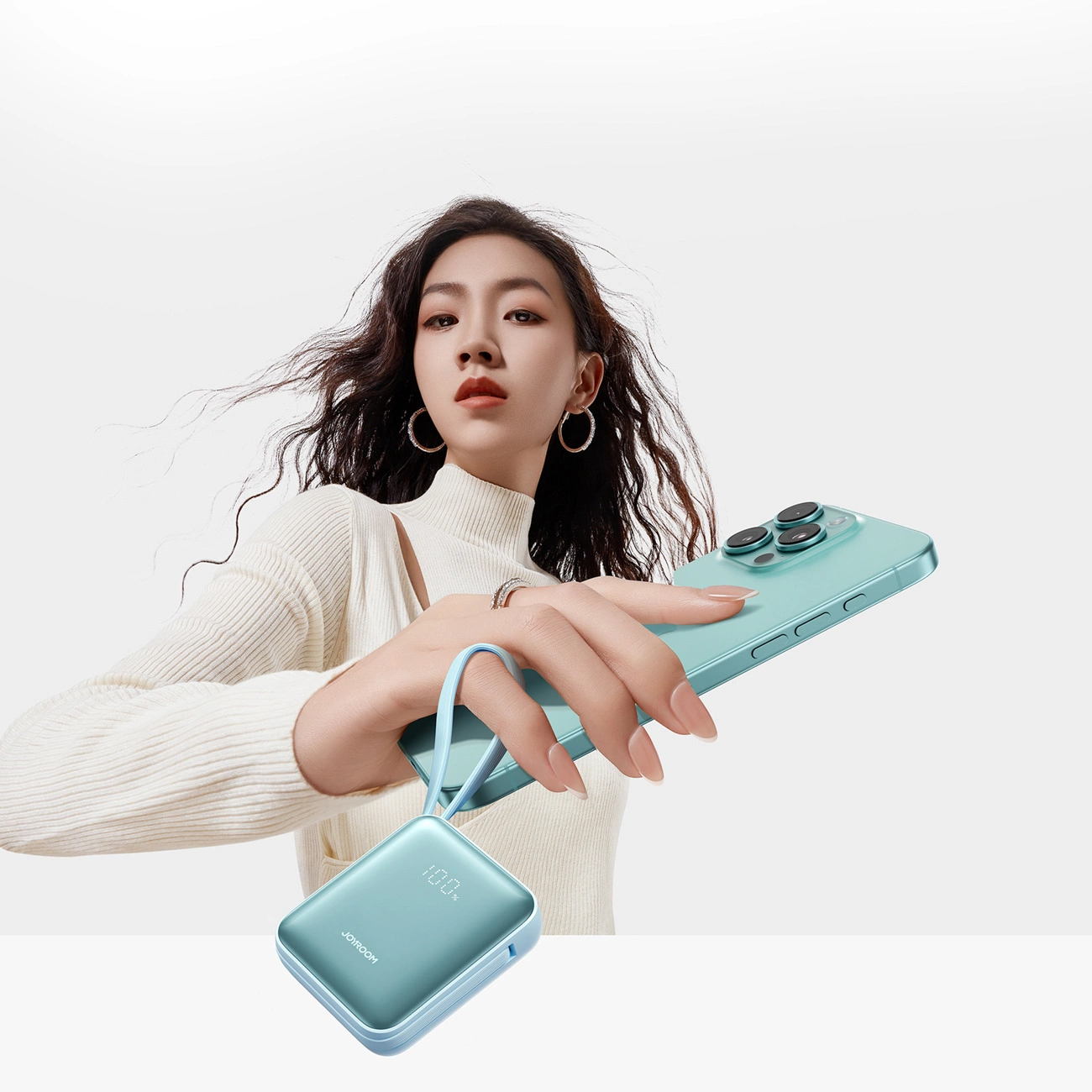 Eine Frau in weißem Pullover hält ein blaues Smartphone und eine Powerbank.