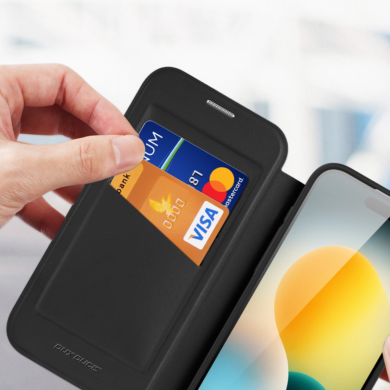Eine Hand schiebt eine Kreditkarte in eine schwarze Handy-Lederhülle.