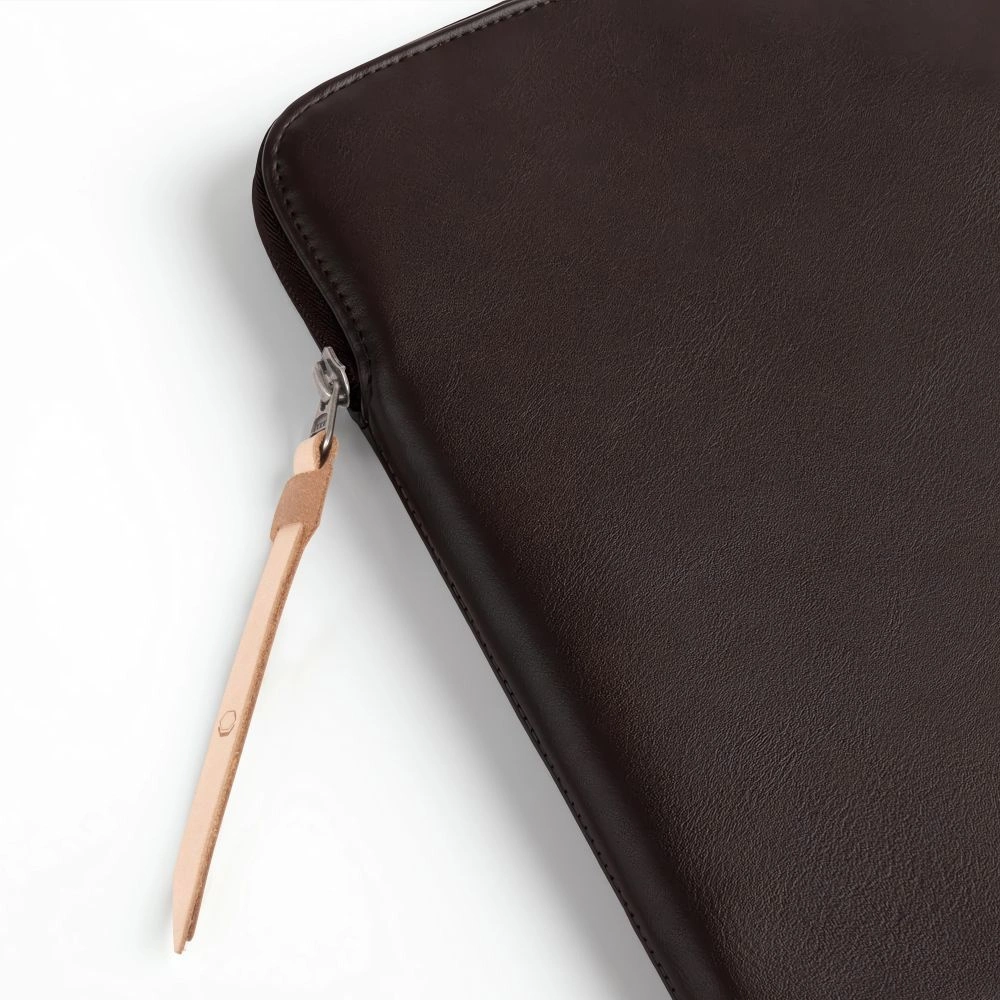 Close-up van een donkerbruine leren laptoptas met een zilveren rits en een lichtbruine treklip.