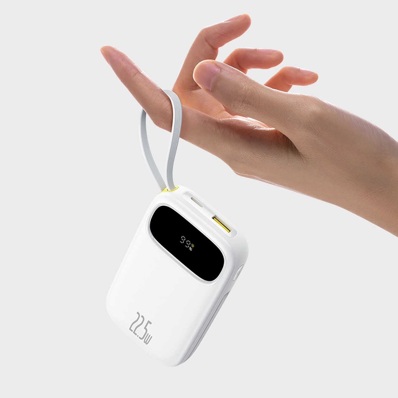 Una mano regge una power bank bianca da 22,5W tramite il suo laccetto su sfondo grigio.