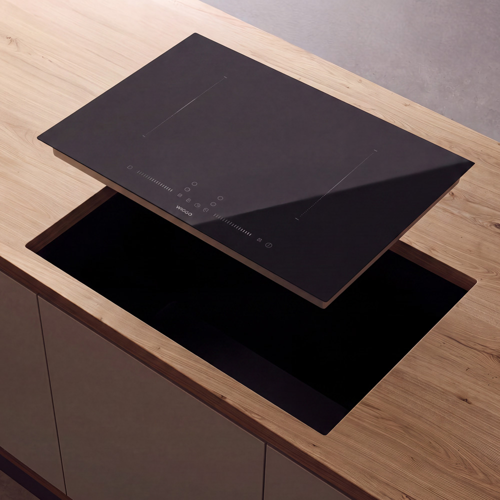 Een zwarte inductiekookplaat die wordt geïnstalleerd in een houten keukenblad.