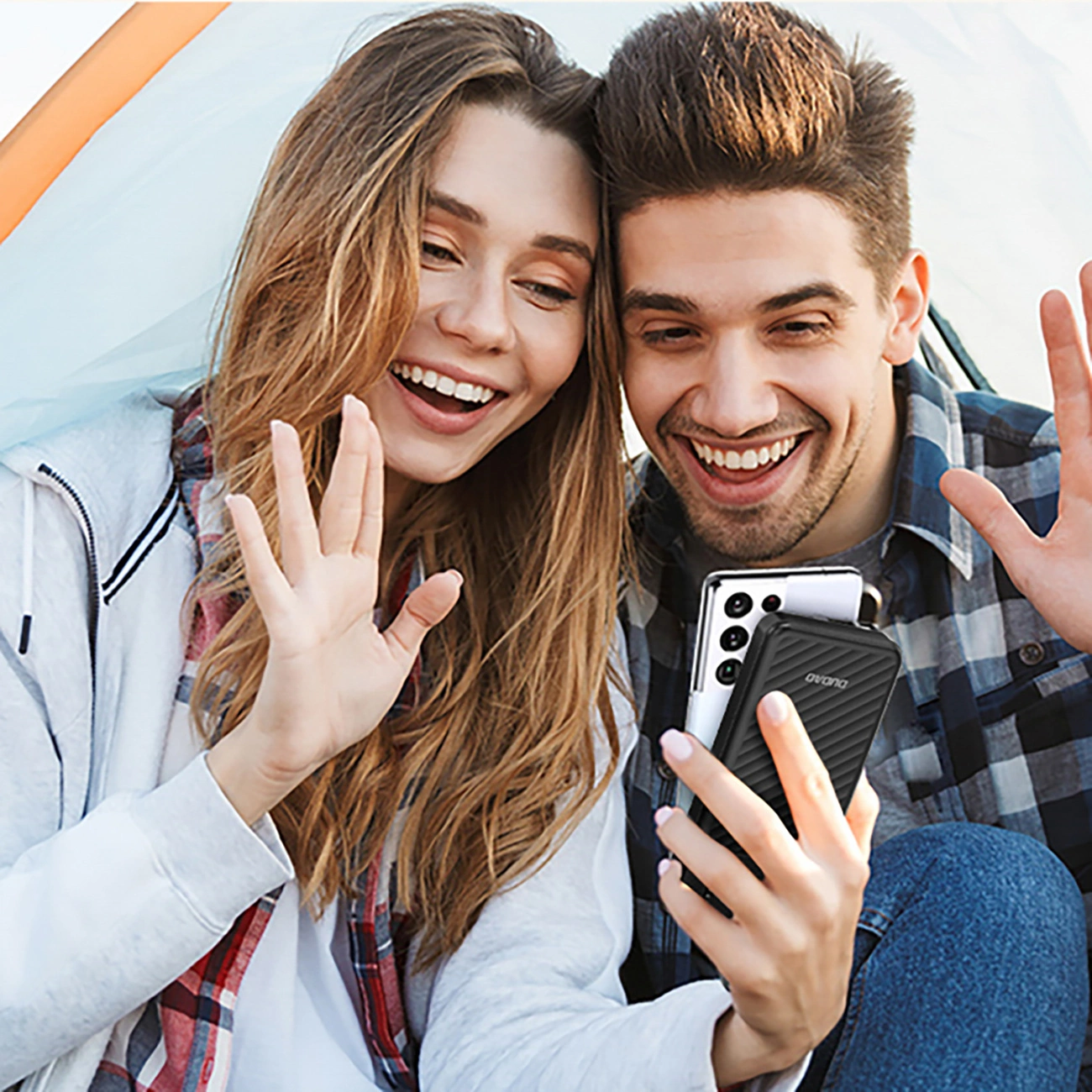 Una giovane coppia sorridente in tenda saluta felicemente durante una videochiamata.