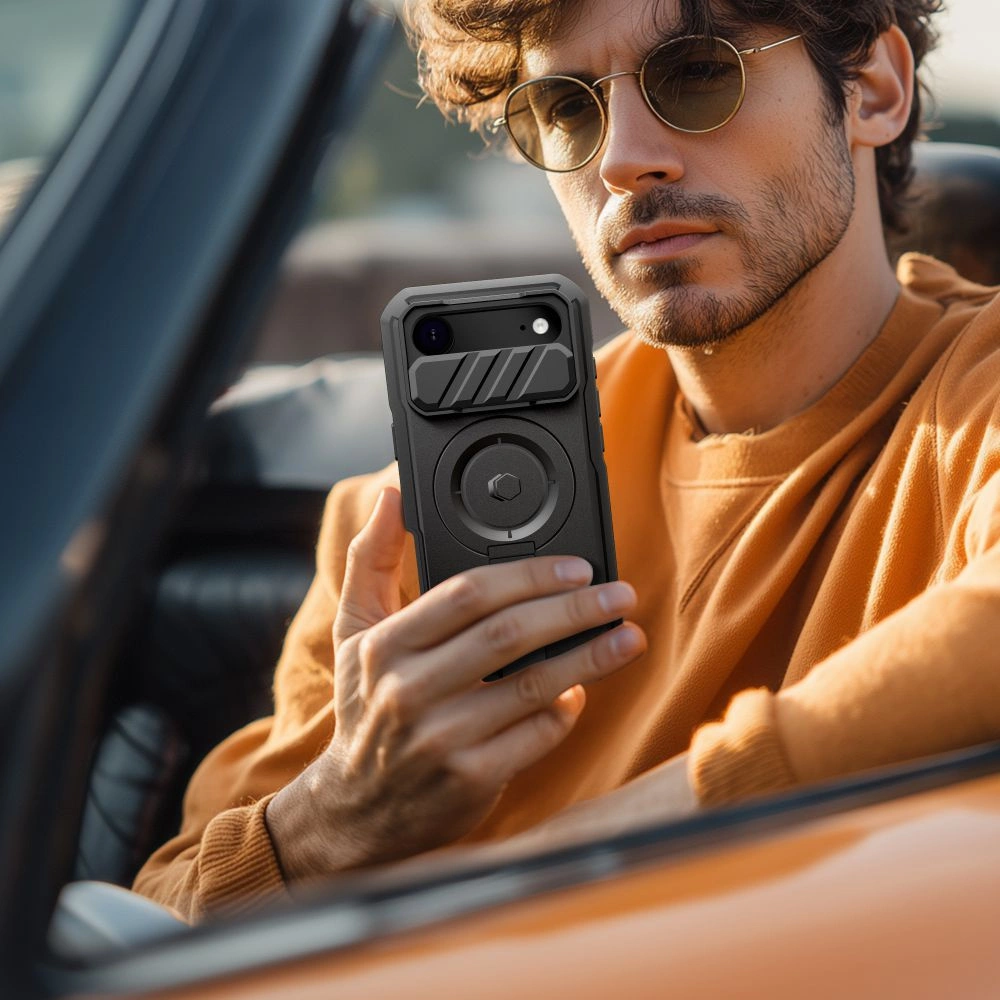 Ein Mann mit Sonnenbrille und gelbem Pullover sitzt in einem Auto und zeigt ein Smartphone mit Schutzhülle.