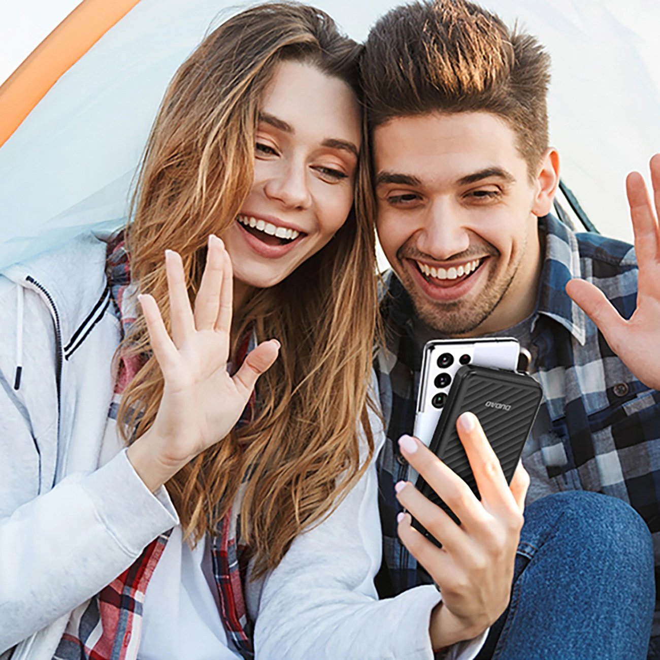 Una giovane coppia sorridente in tenda che saluta e fa una videochiamata.
