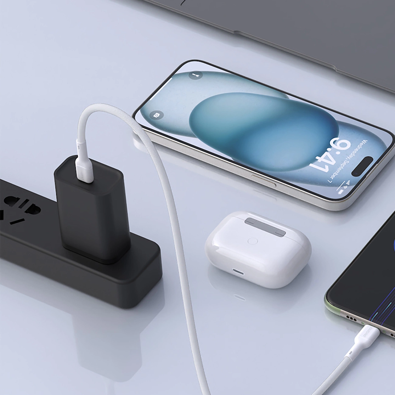 Eine schwarze Steckdosenleiste mit eingestecktem Ladegerät, verbunden mit Smartphone und Ohrhörern auf einem Tisch.