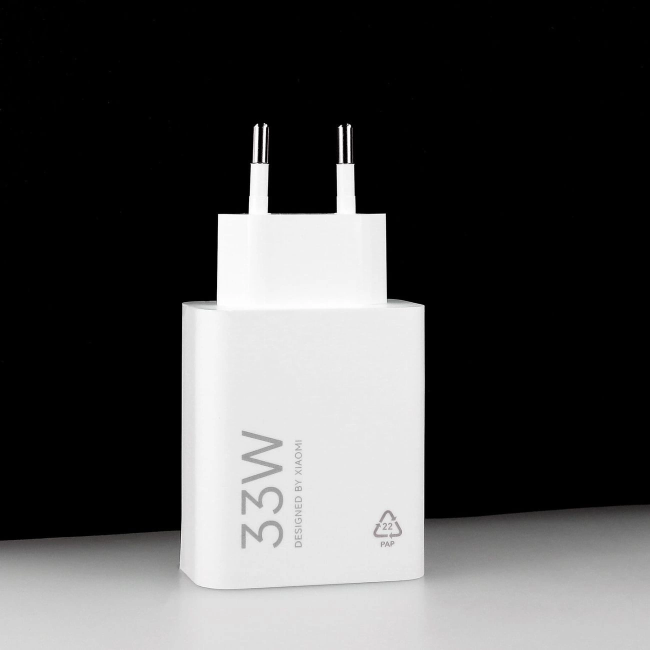 Un caricabatterie da muro Xiaomi 33W bianco su superficie bianca e sfondo nero.