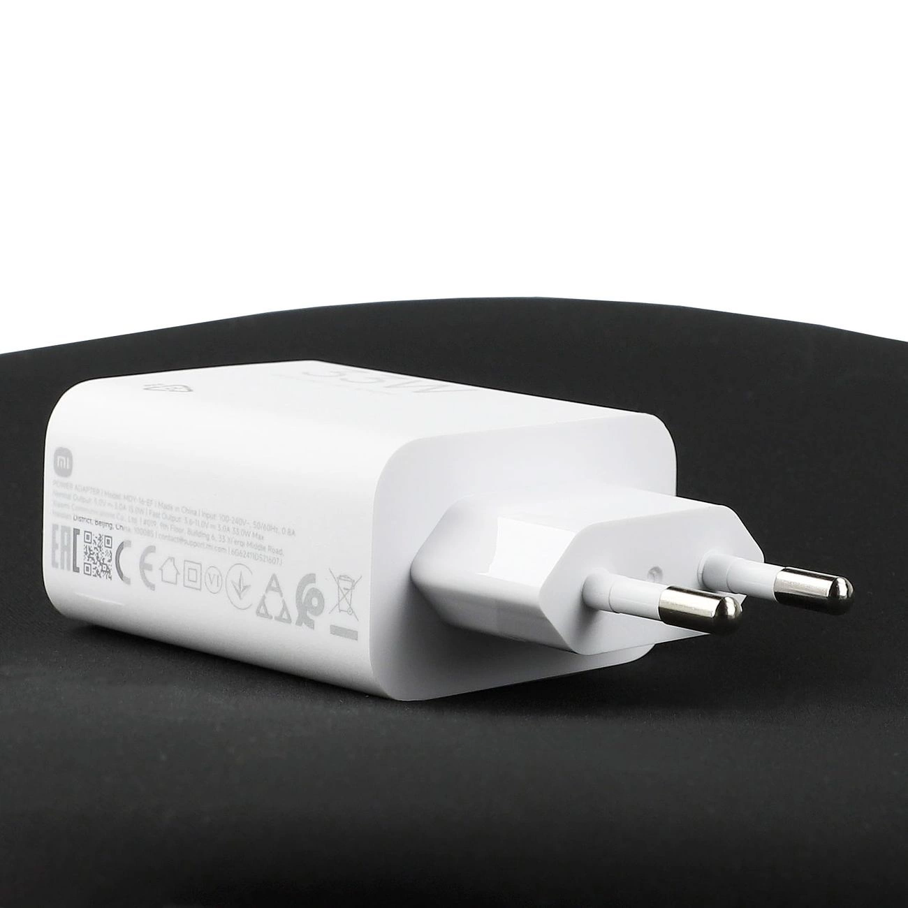 Un alimentatore Xiaomi bianco con due poli poggiato su una superficie scura.