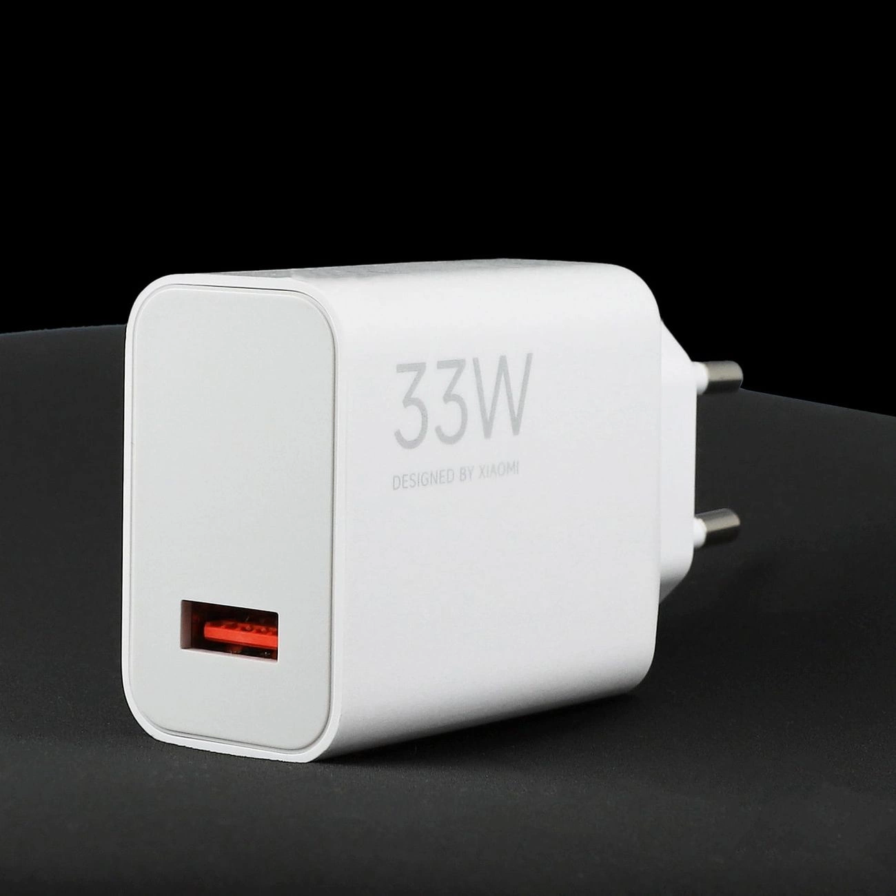 Un caricabatterie rapido bianco Xiaomi da 33W con una porta USB rossa su una superficie scura.