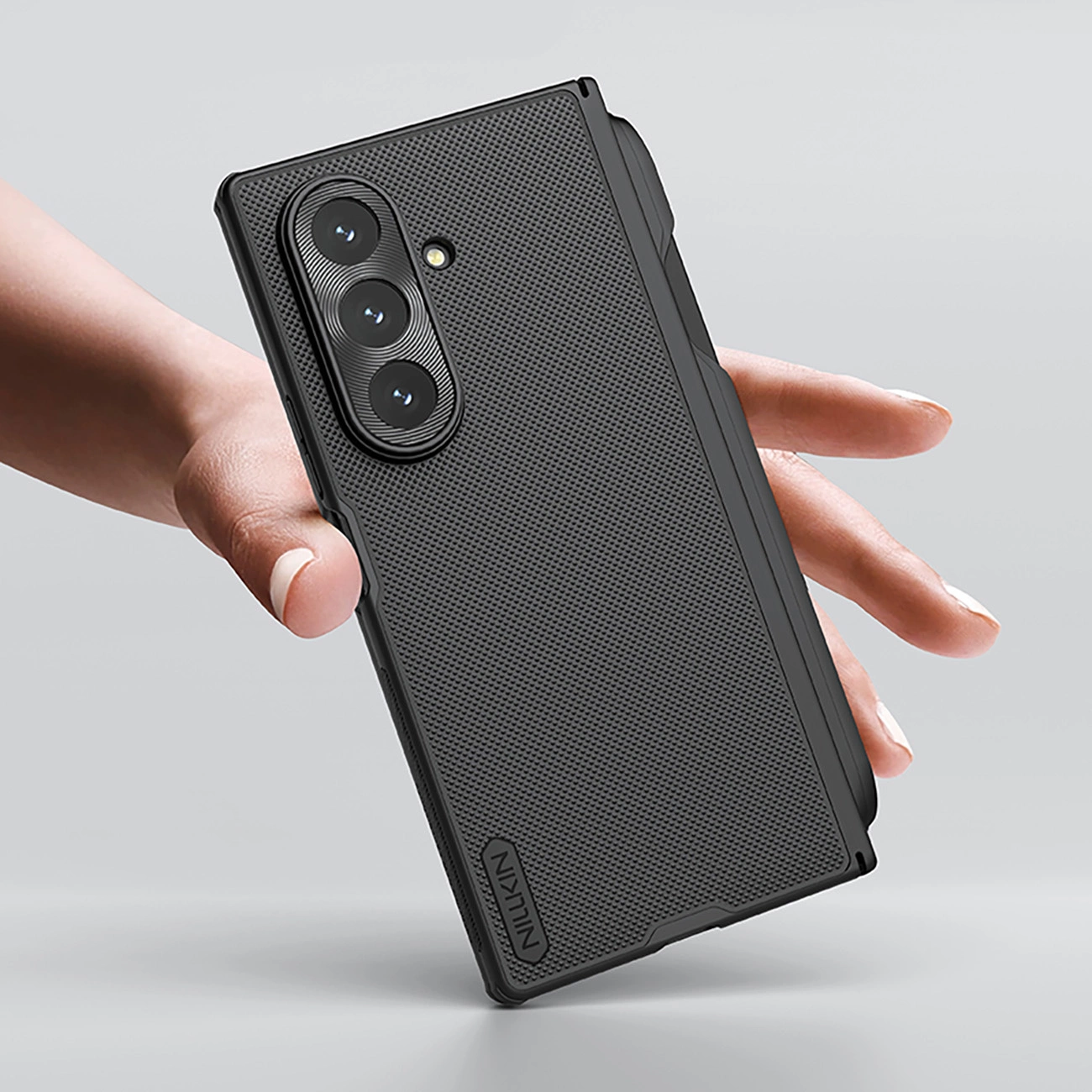 Eine Hand hält ein schwarzes Smartphone mit strukturierter Hülle und dreifacher Kamera auf grauem Hintergrund.