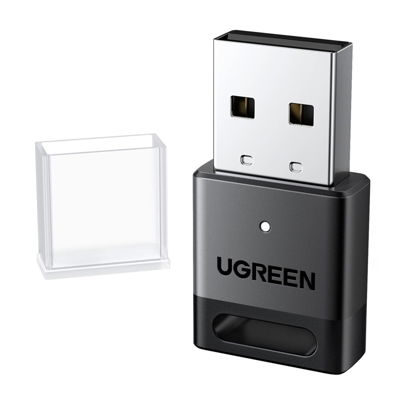 Un adattatore USB Ugreen nero con connettore in metallo e cappuccio protettivo trasparente accanto su sfondo bianco.