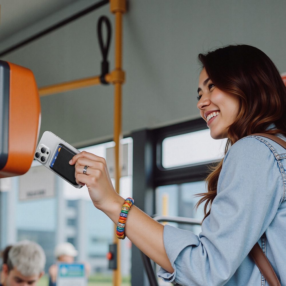 Eine lächelnde Frau bezahlt die Fahrt in einem Bus, indem sie ihr Smartphone an ein orangefarbenes Lesegerät hält.
