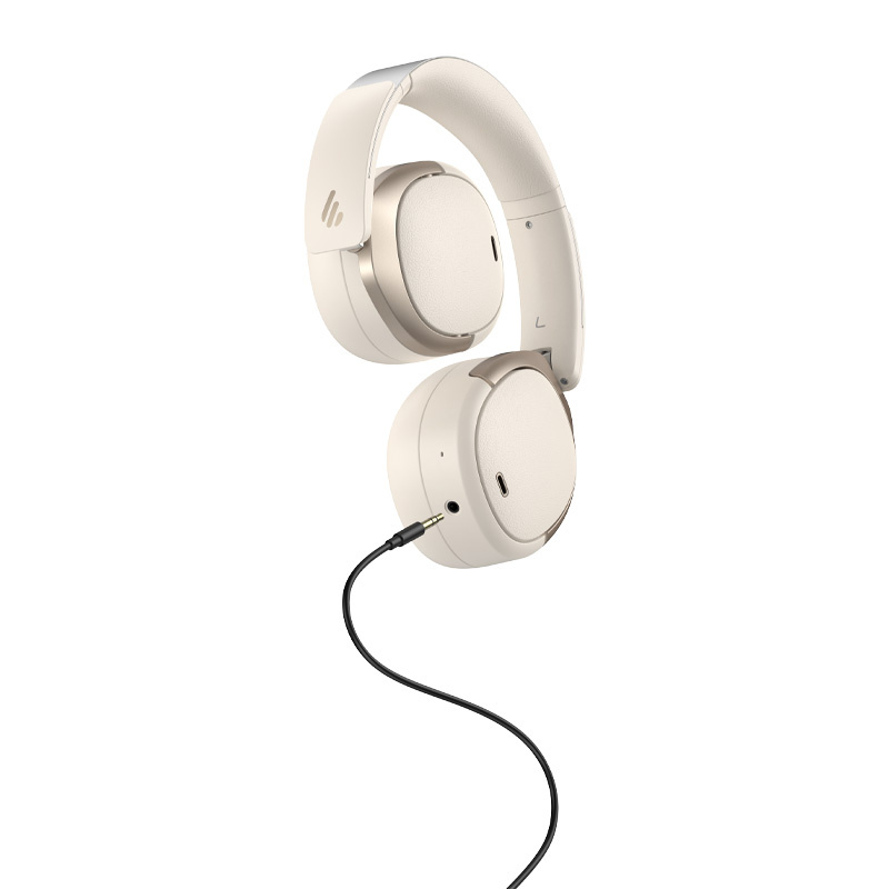 Cuffie over-ear beige con dettagli dorati, collegate a un cavo audio nero, su sfondo bianco.