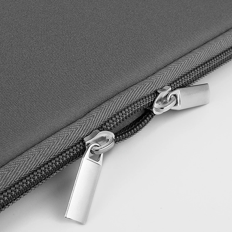 Primo piano di una borsa in tessuto grigio con due cerniere argentate su sfondo chiaro.