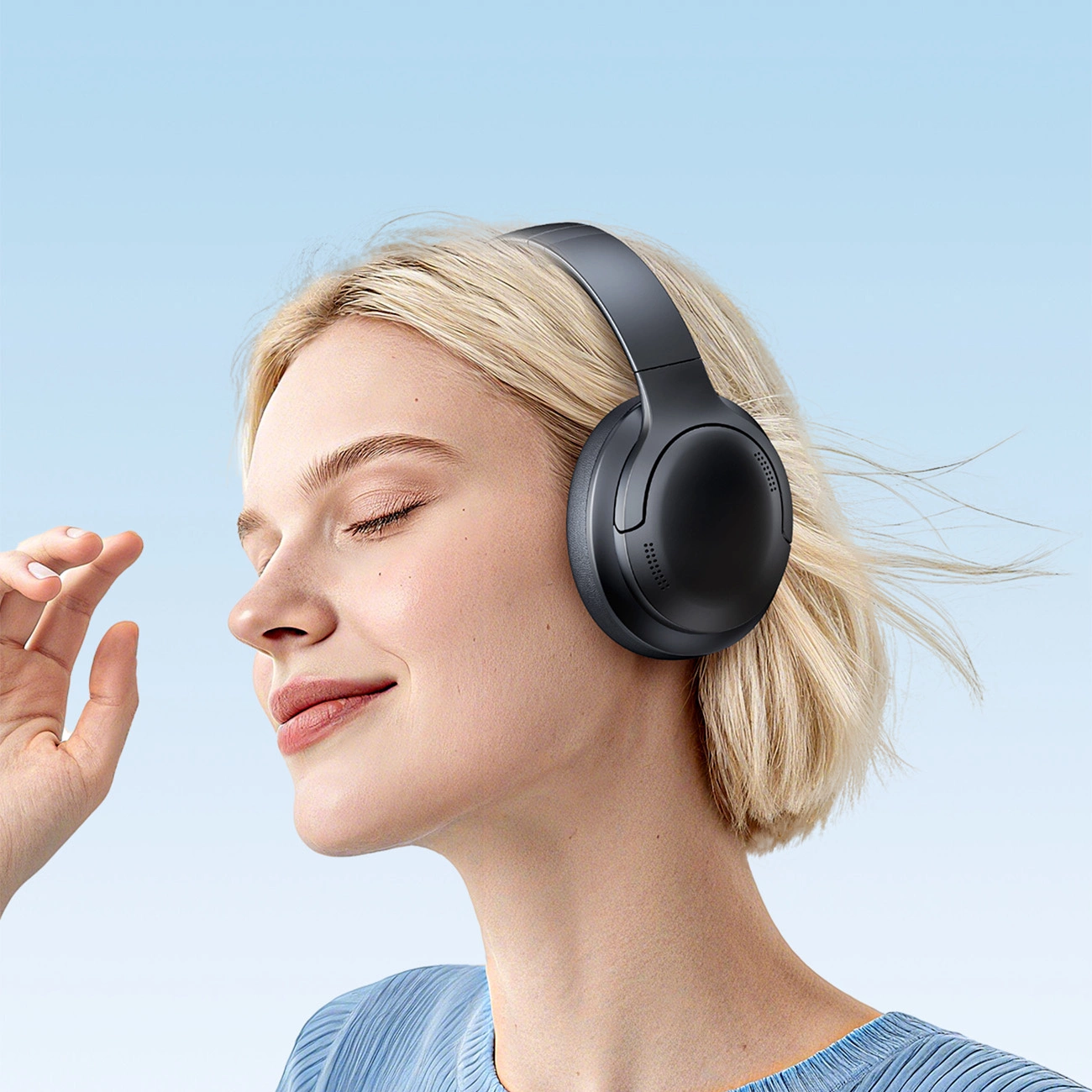 Una donna bionda con gli occhi chiusi indossa cuffie over-ear nere su sfondo azzurro.