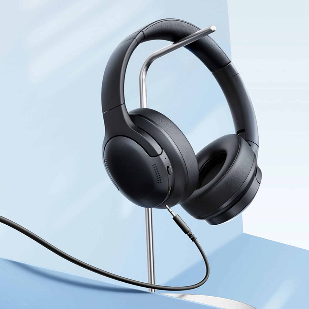 Cuffie over-ear nere su supporto argentato con cavo audio collegato su sfondo azzurro.