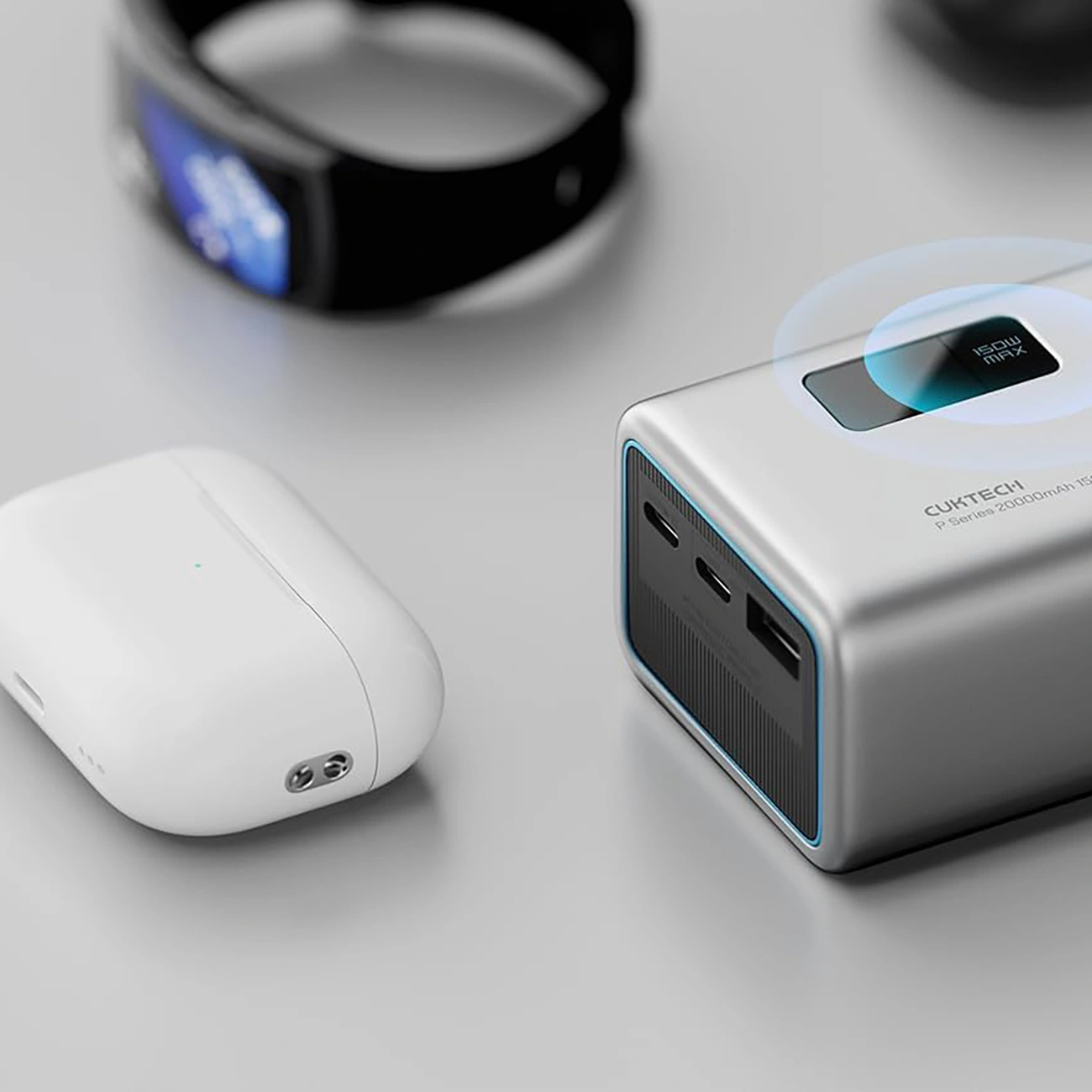 Un power bank argentato, auricolari bianchi in una custodia di ricarica e uno smartwatch nero su una superficie.