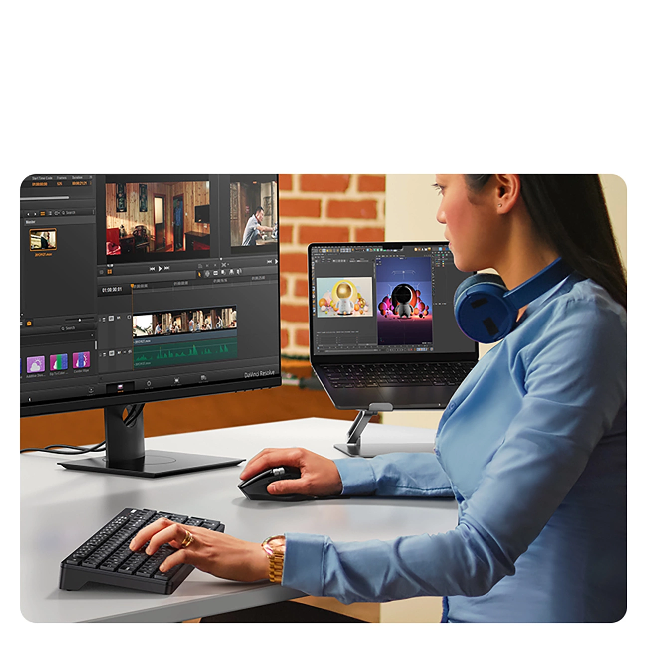 Una donna con camicia blu e cuffie monta video su un computer e un portatile alla scrivania.