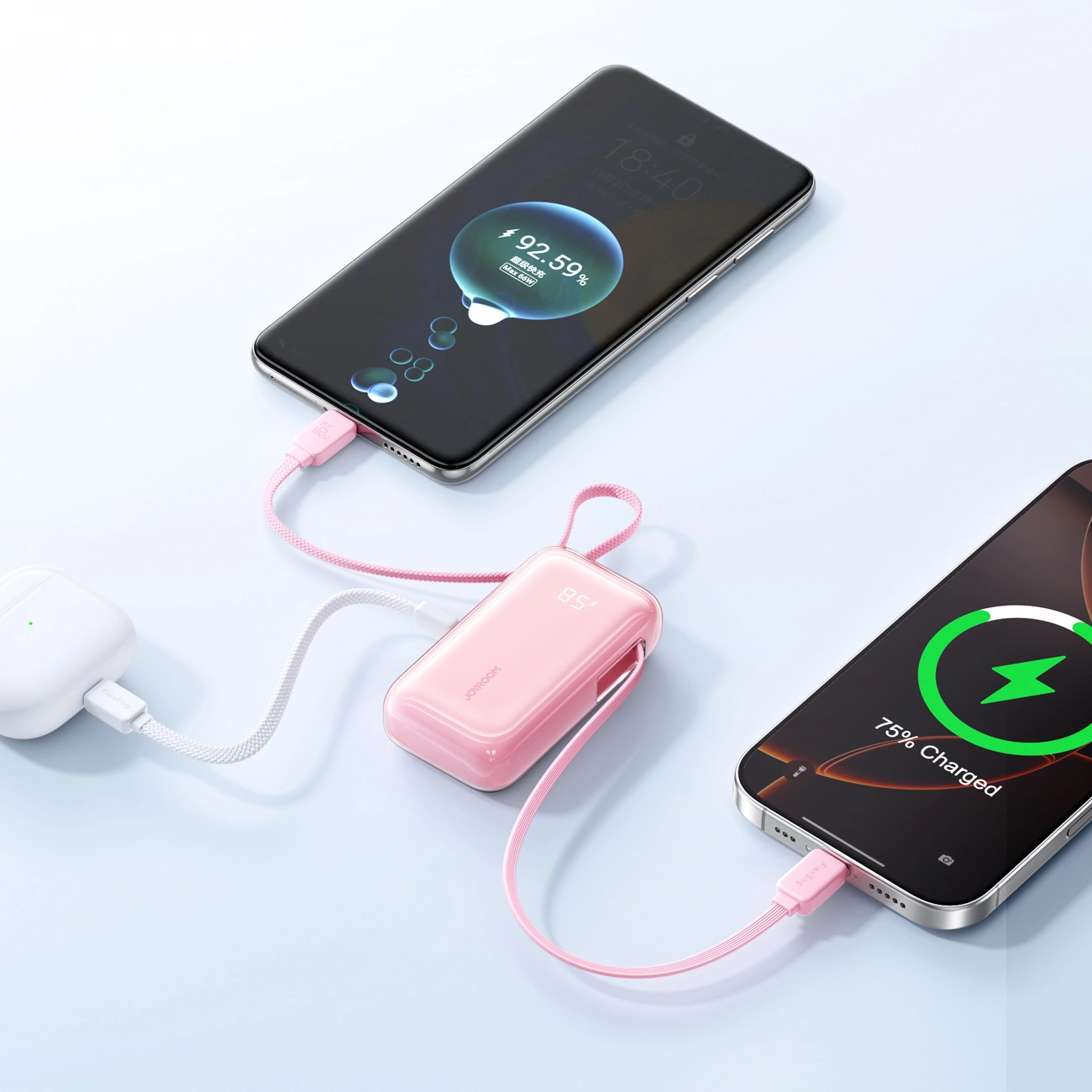Une batterie externe rose charge deux smartphones et un boîtier blanc sur fond clair.