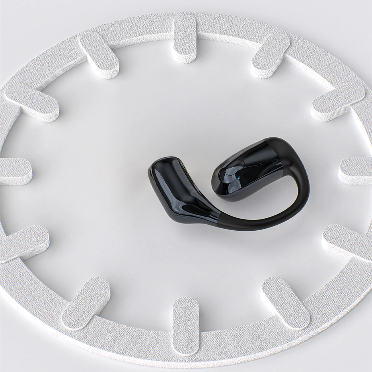 Un auricolare wireless nero poggia su una superficie bianca all'interno di un anello bianco.