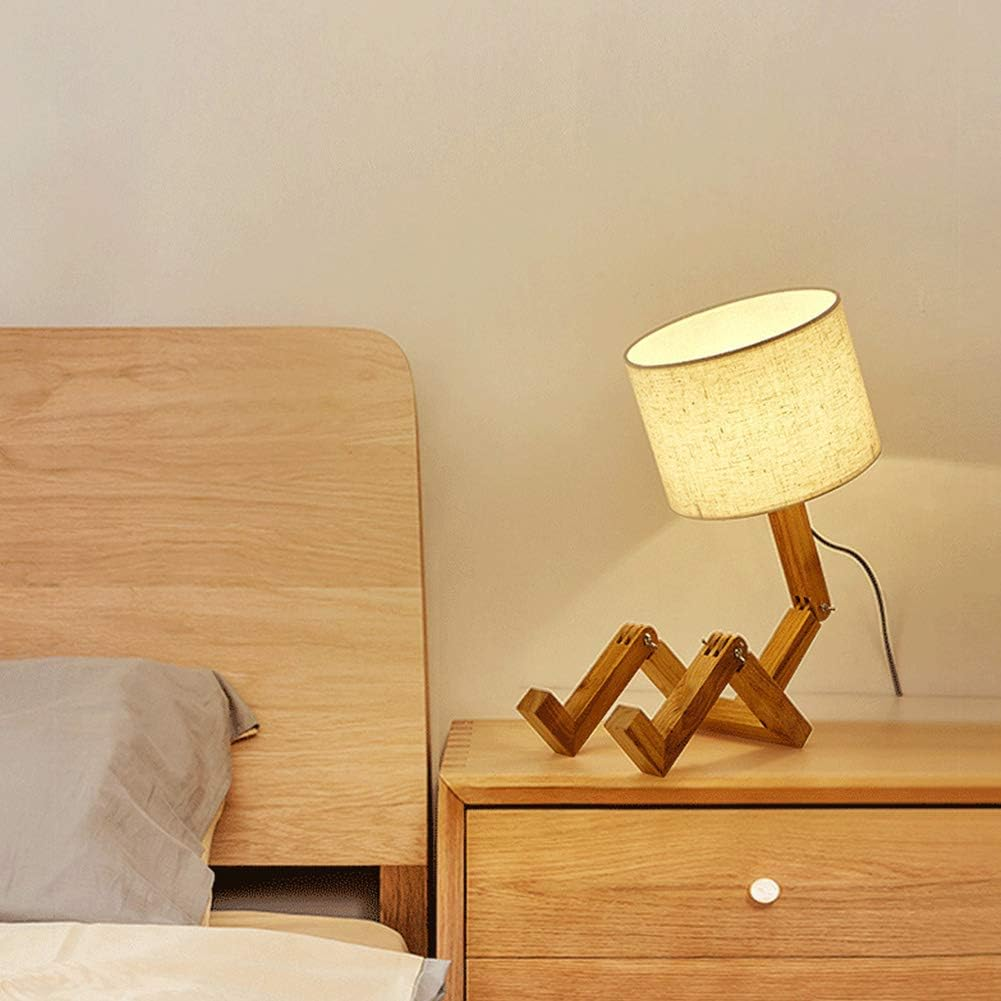 Eine hölzerne Roboterlampe mit Stoffschirm steht auf einem Nachttisch neben einem Bett.