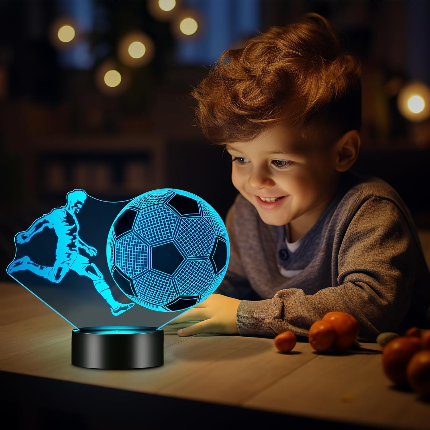 Ein glücklicher Junge betrachtet eine blau leuchtende 3D-Fußball-LED-Lampe auf einem Tisch in einem abgedunkelten Raum.