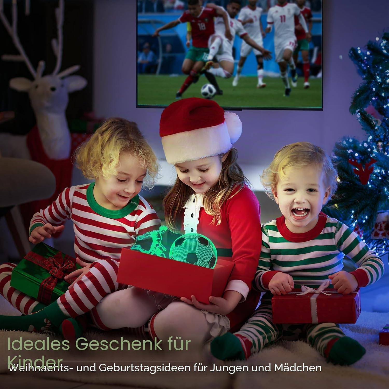 Drei Kinder öffnen Geschenke vor einem Fernseher mit einem Fußballspiel.
