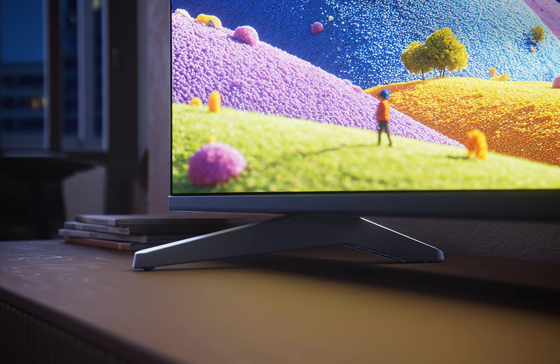 Un televisor en una mesa muestra una pantalla de paisaje fantástico colorido con una figura pequeña.