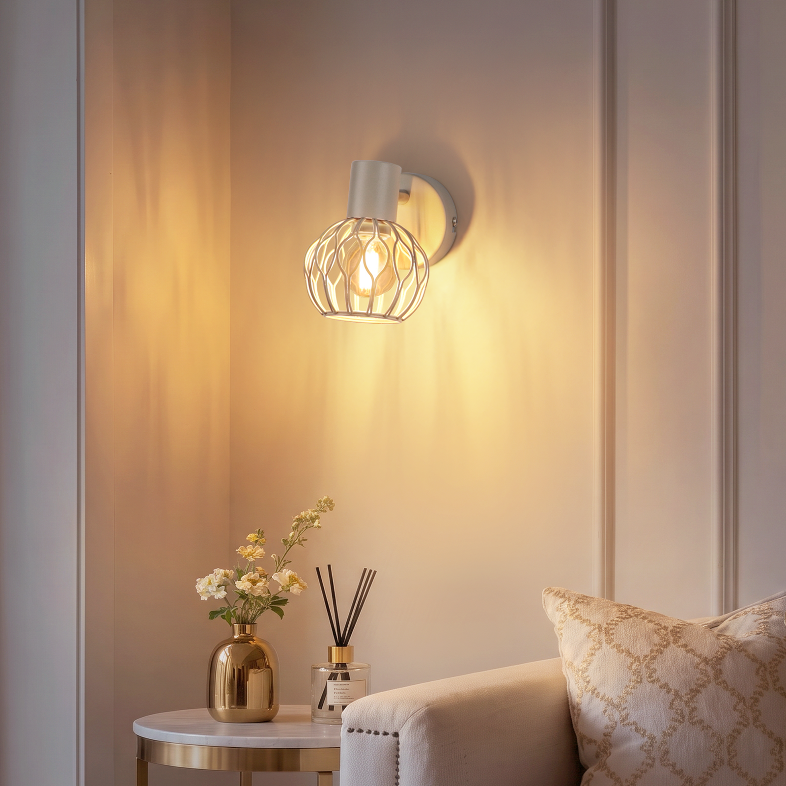 Una lámpara de pared con luz cálida sobre una mesita con flores y un sofá.