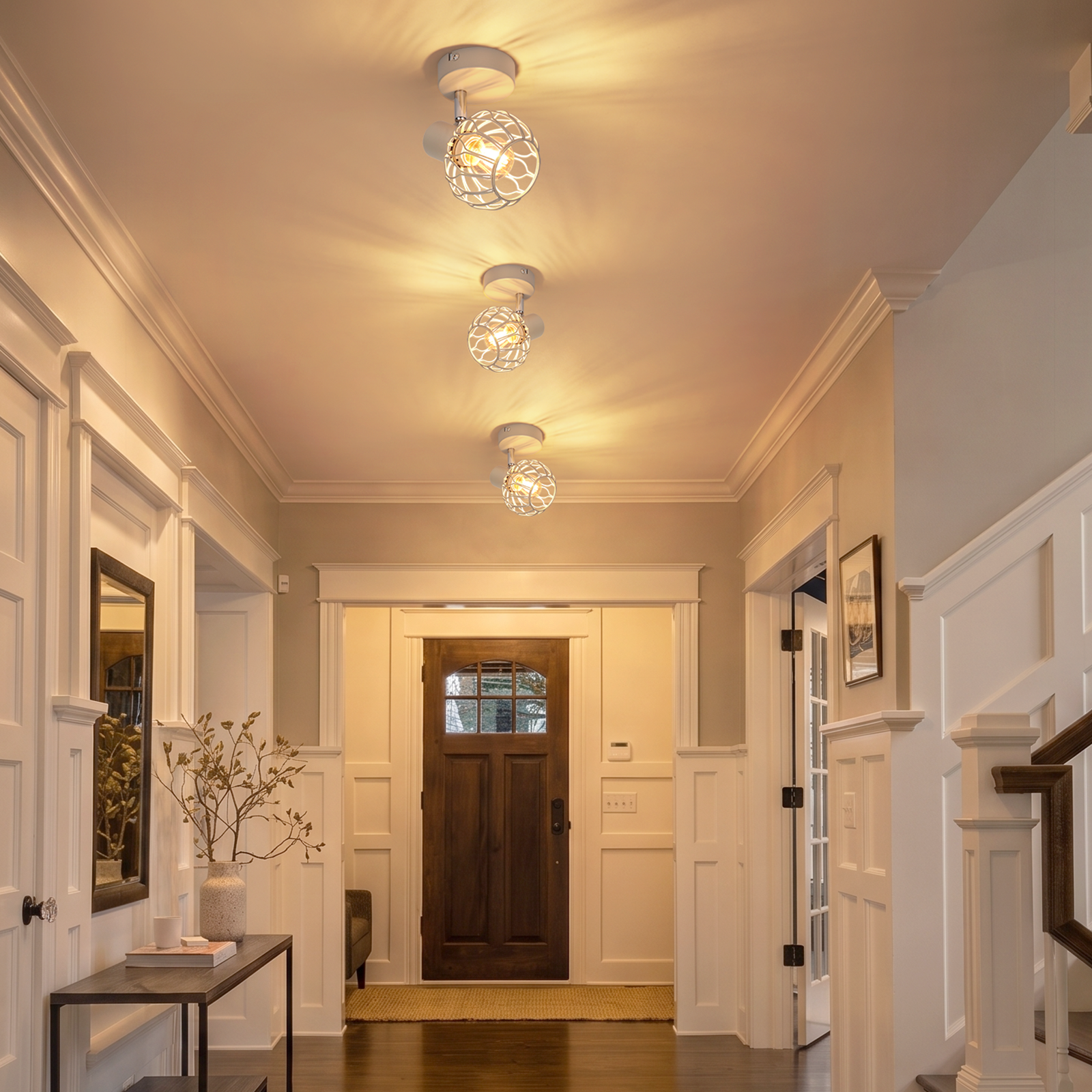 Un pasillo luminoso con tres lámparas de techo esféricas, una puerta principal de madera oscura y paneles blancos.