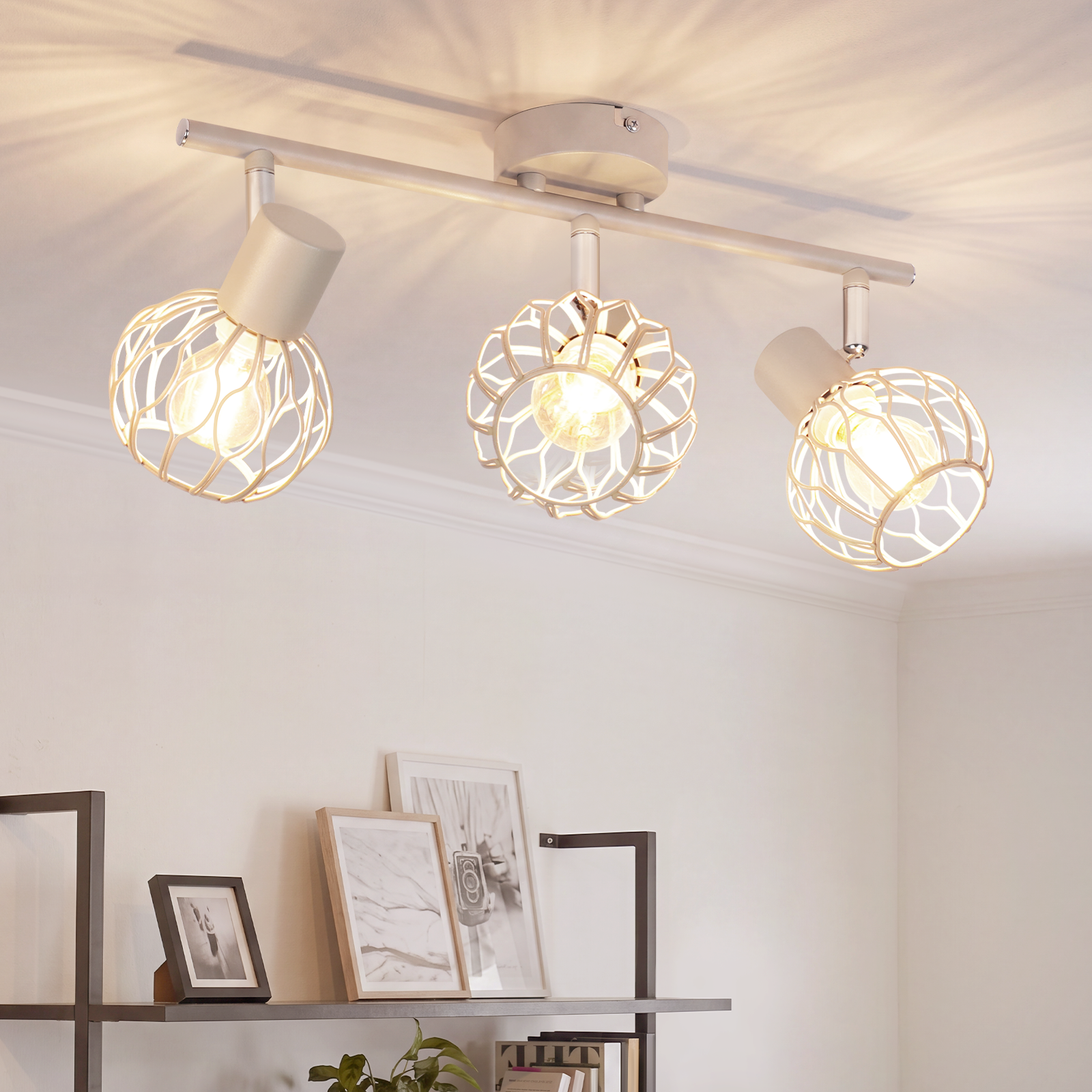 Eine weiße Deckenlampe mit drei Drahtgeflechtkugeln wirft Licht an eine weiße Wand und Regale.