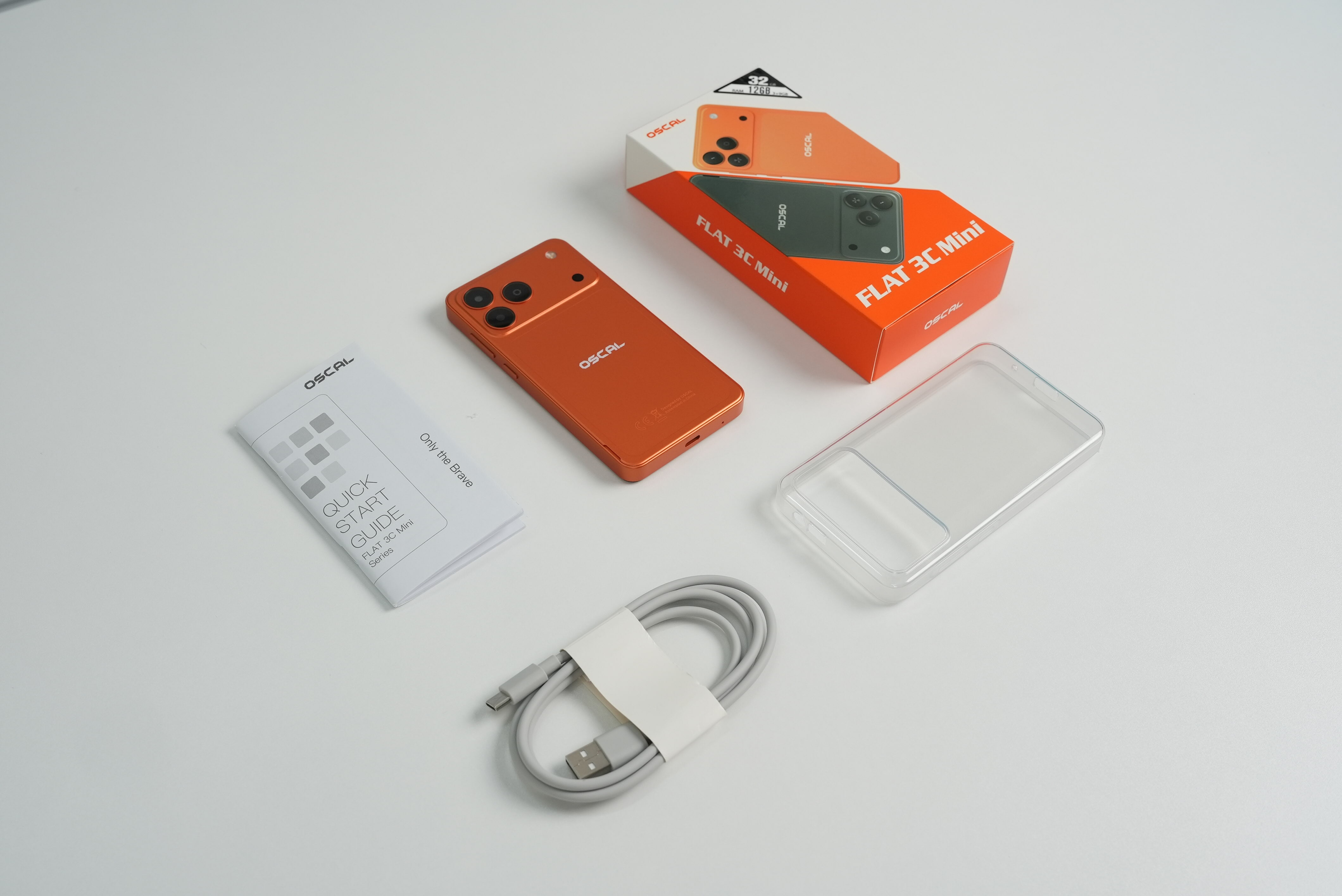 Ein orangefarbenes Oscal Flat 3C Mini Smartphone mit Box, Anleitung, Ladekabel und Hülle auf weißem Tisch.