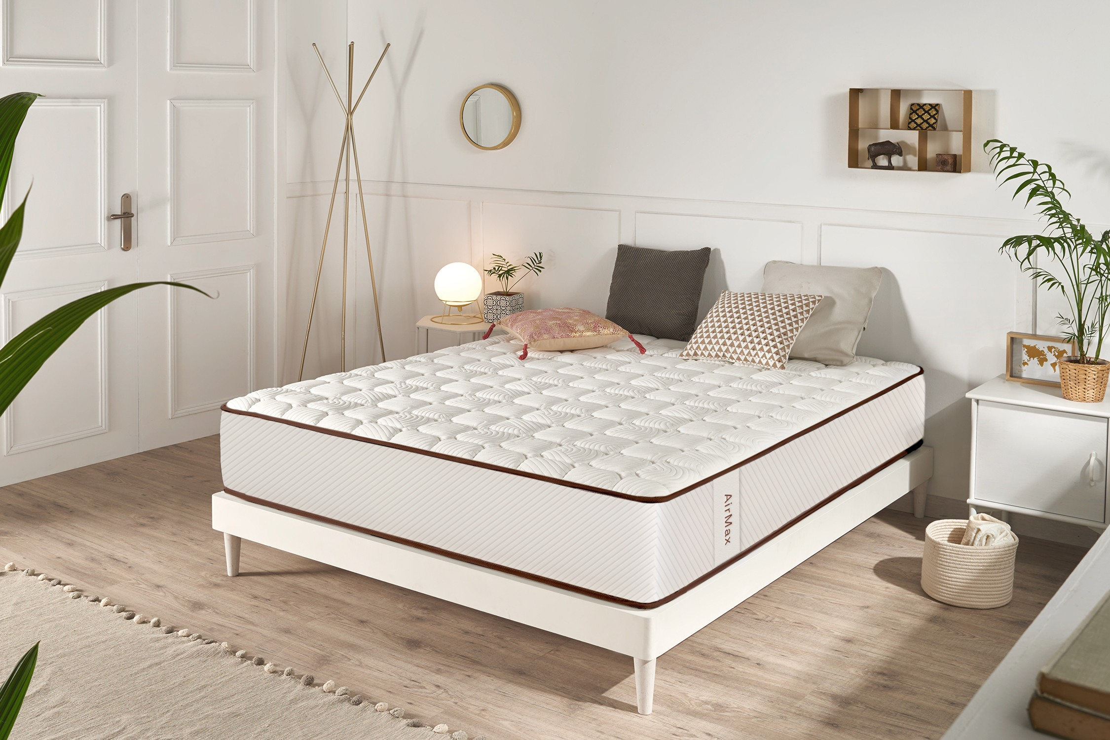 Un colchón blanco en una cama moderna en un dormitorio luminoso con paredes blancas, piso de madera y plantas.