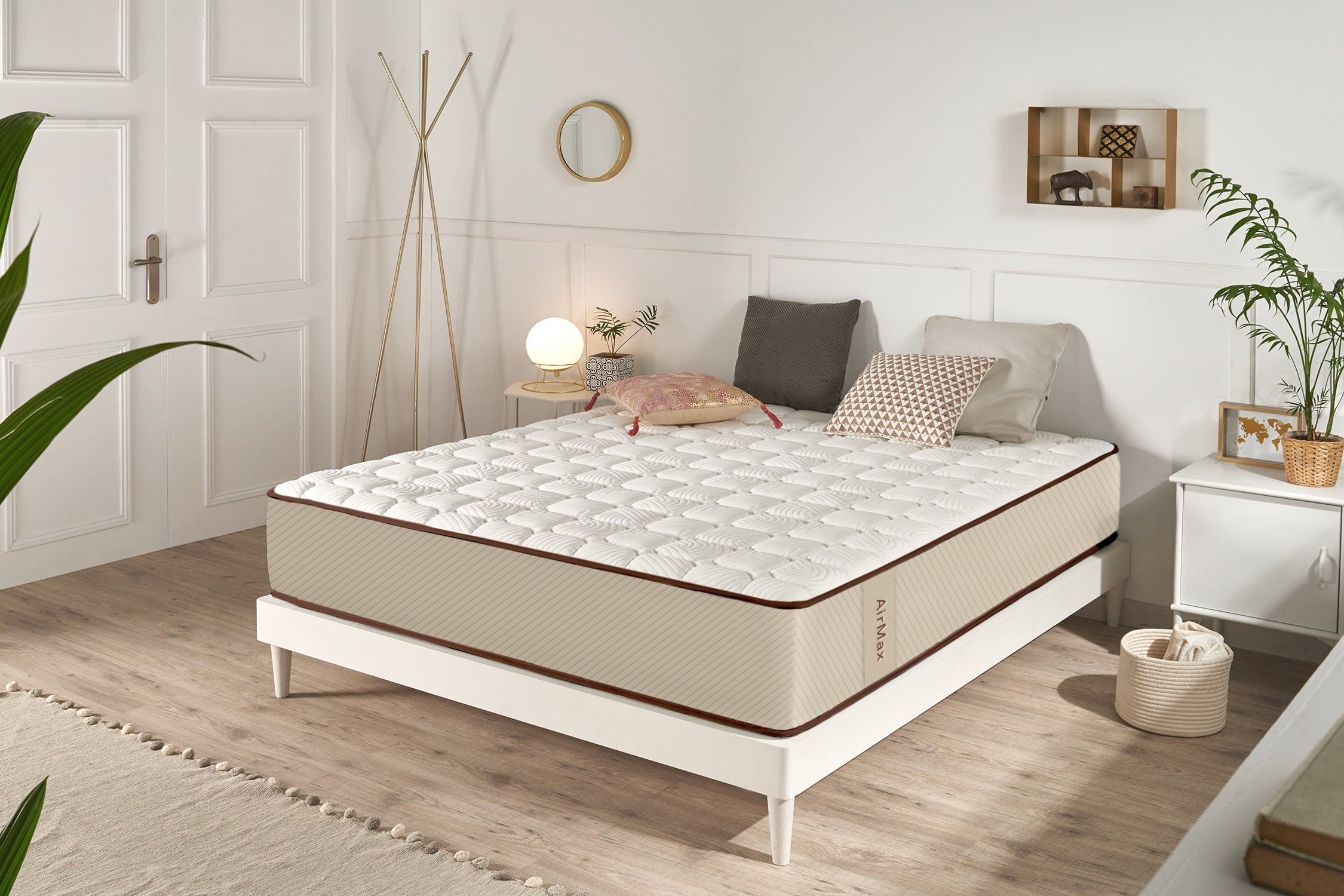 Cama blanca con colchón acolchado y cojines en un dormitorio moderno y luminoso con plantas.
