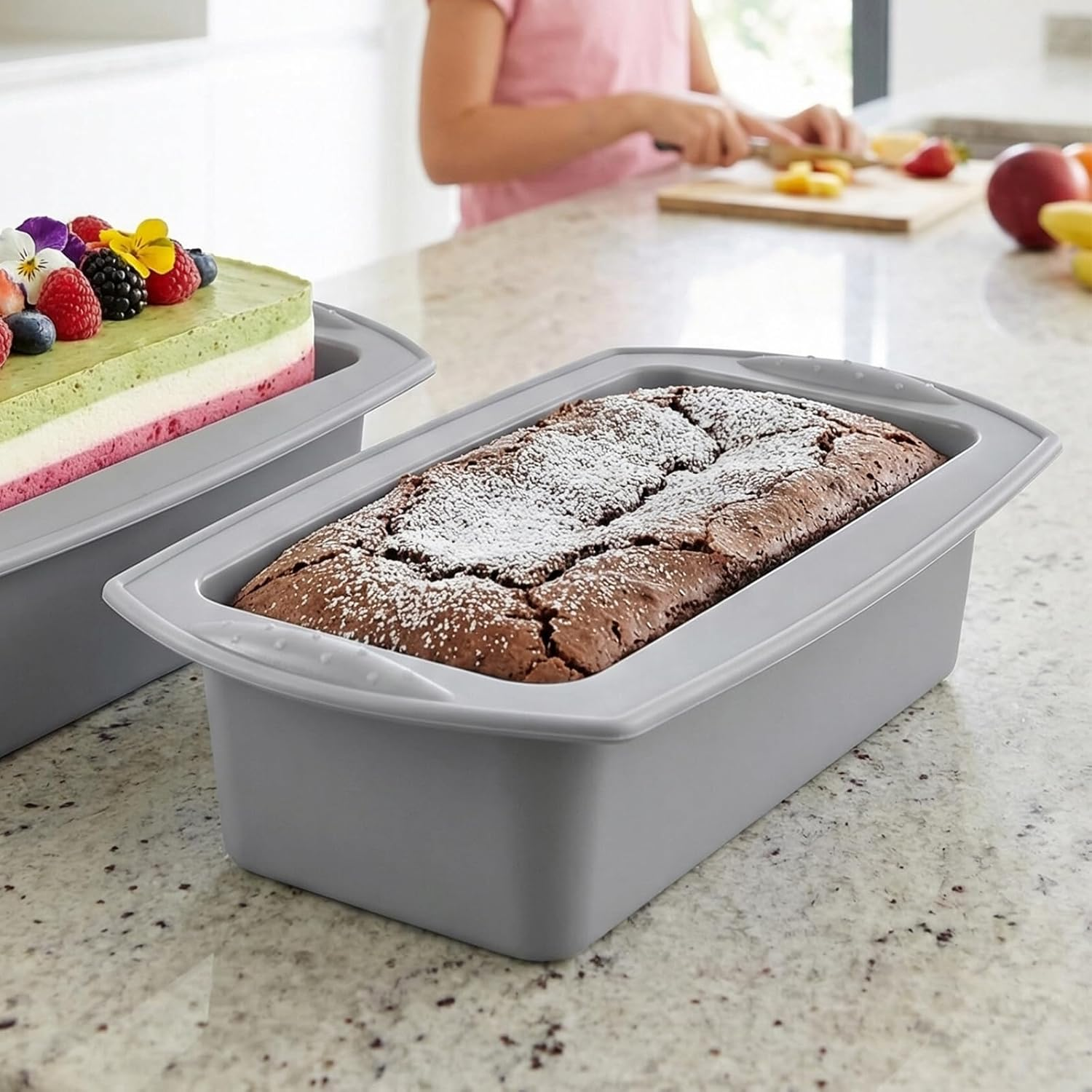 Ein gebackener Schokoladenkuchen mit Puderzucker in einer grauen Silikonform auf einer Küchentheke.