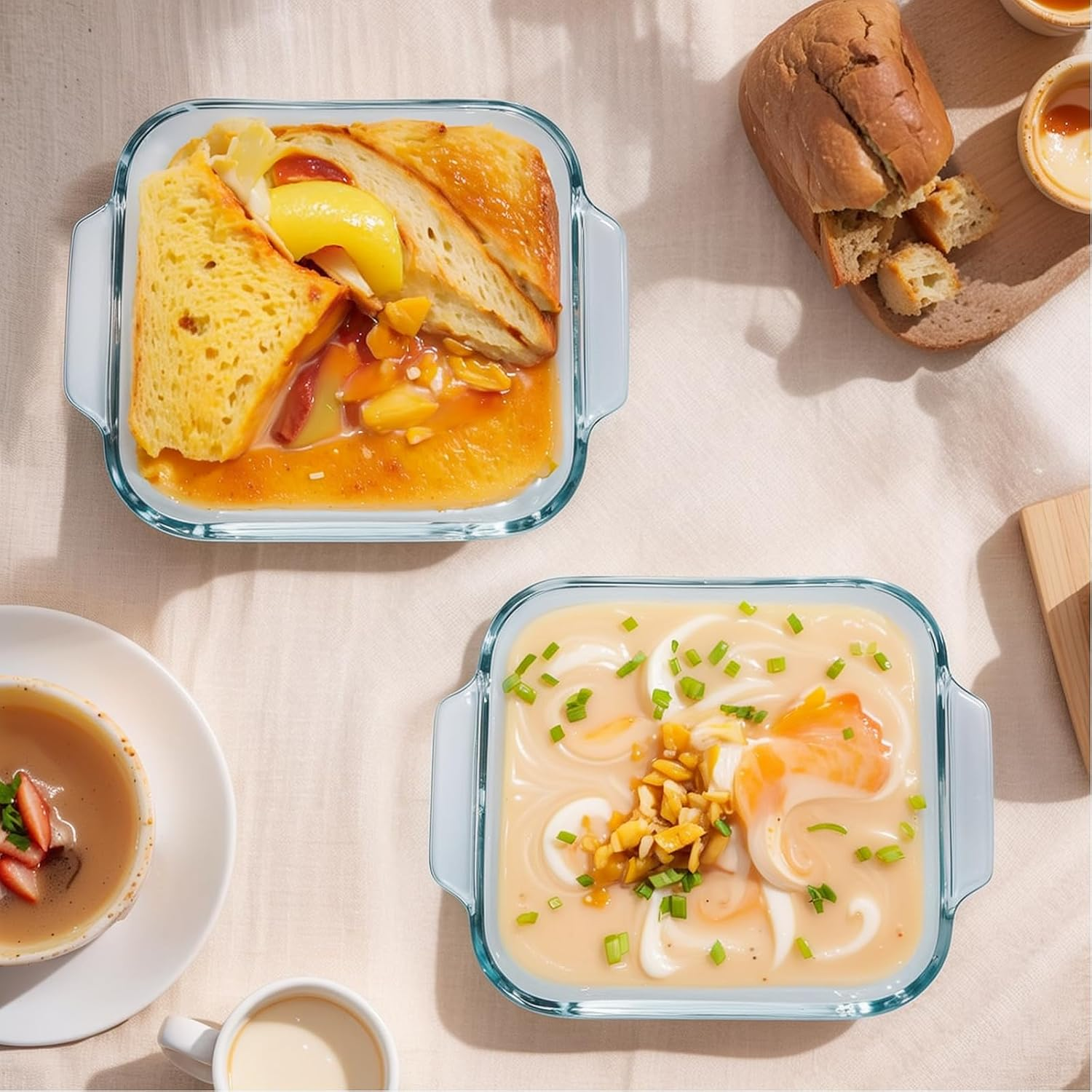 Zwei Glastöpfe mit Speisen, Brot und Suppe auf hellem Tisch.