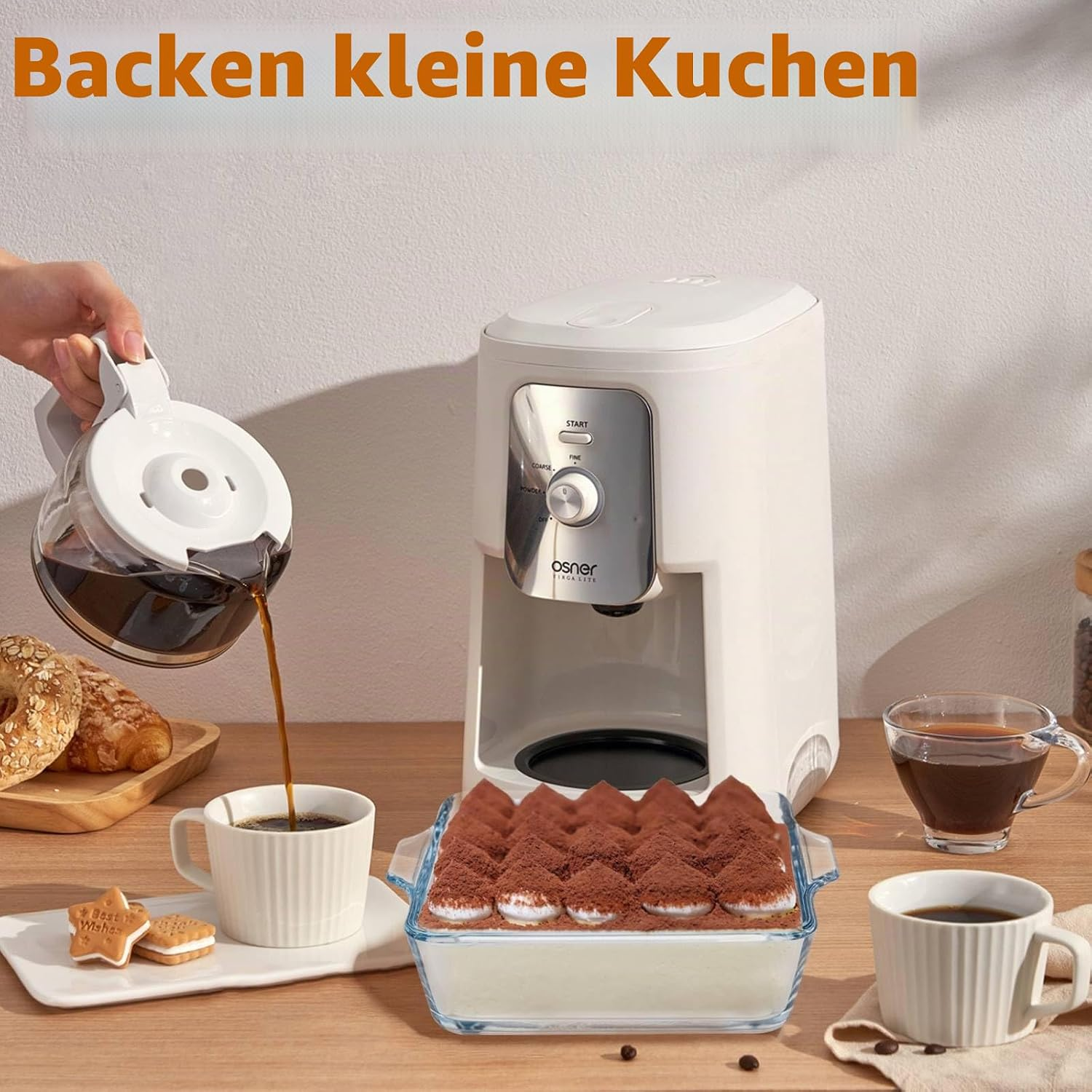 Eine Hand gießt Kaffee in eine weiße Tasse neben Kaffeemaschine, Tiramisu und Gebäck.