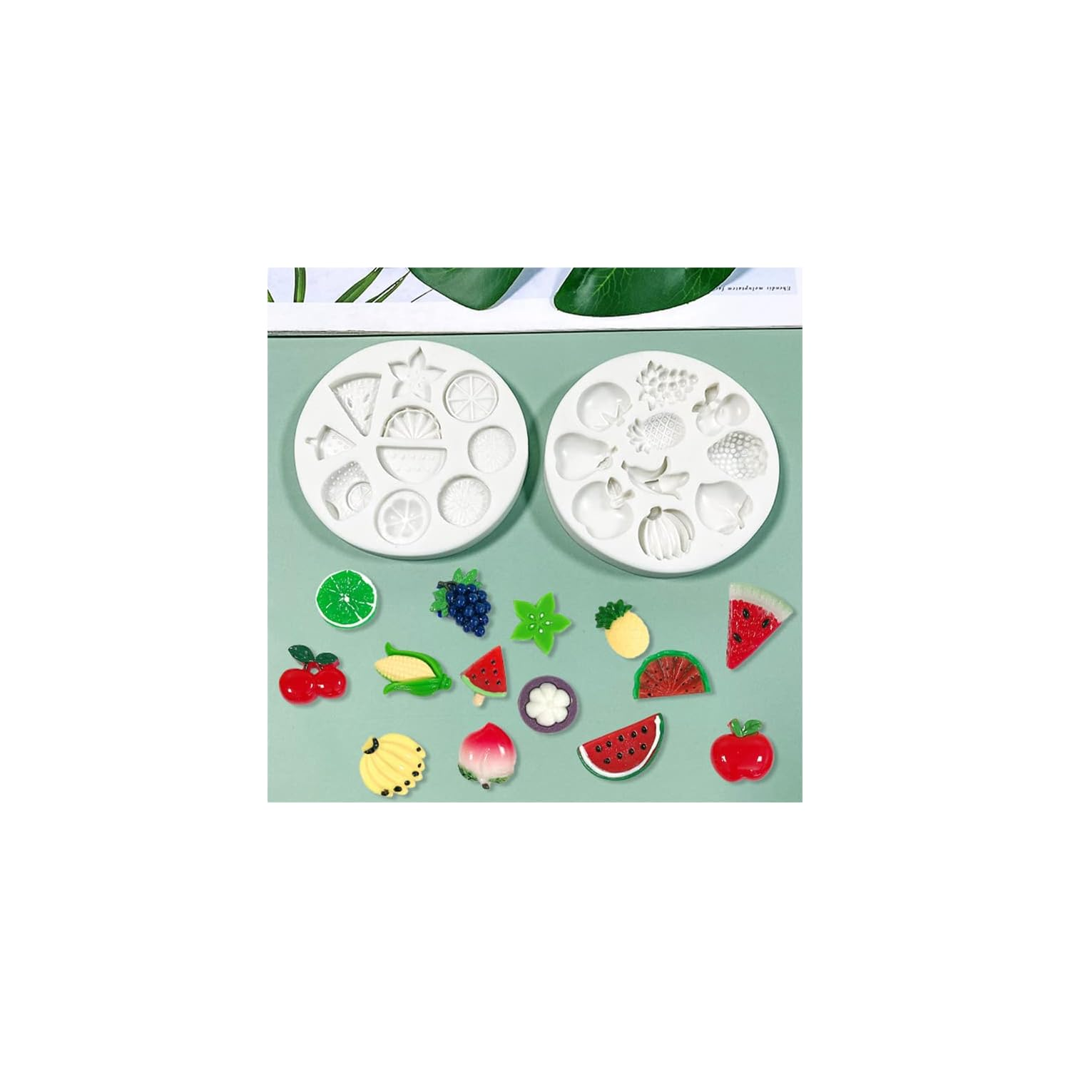 Zwei runde weiße Silikonformen und bunte Frucht-Miniaturen auf grünem Hintergrund.