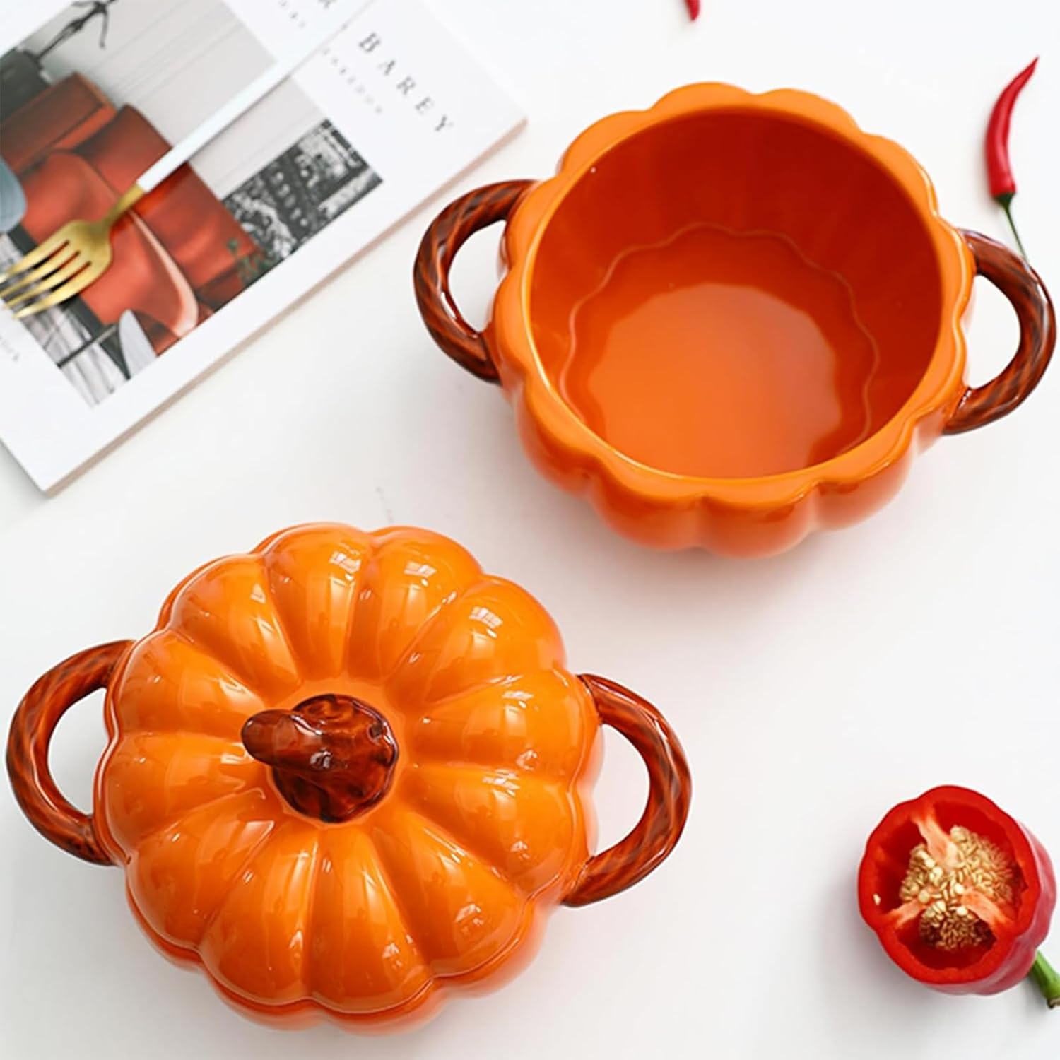 Zwei orange Kuerbisschruessel mit Braunen Griffen, ein Deckel und rote Chilischoten auf weissem Grund.