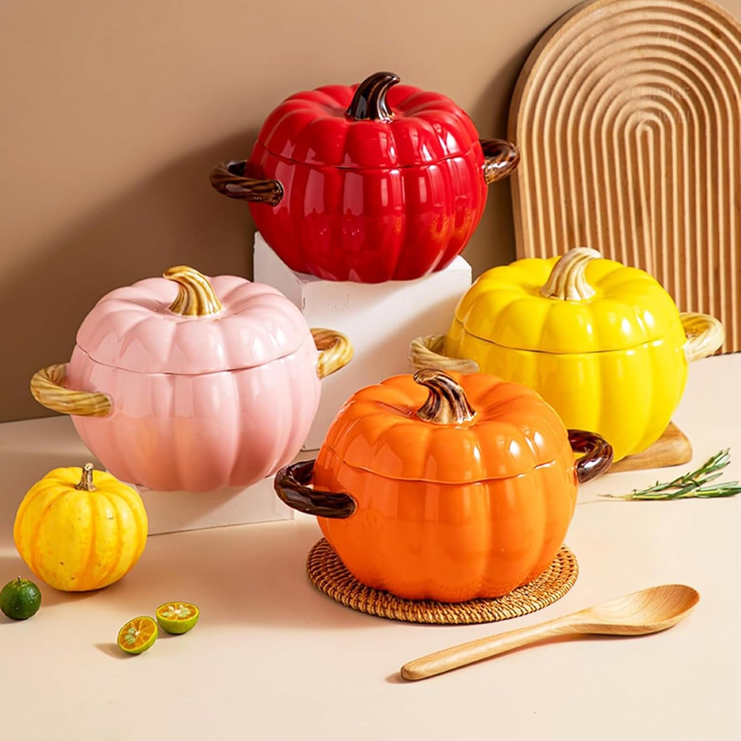 Vier Kürbistöpfe in Rot, Rosa, Gelb und Orange mit kleinen Kürbissen und einem Holzlöffel auf einem Tisch.