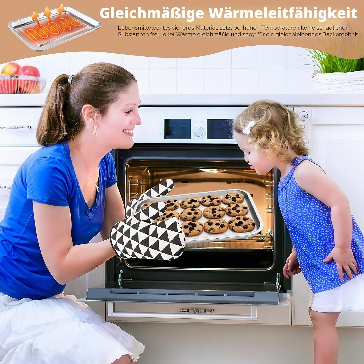 Eine Frau mit Ofenhandschuhen und ein kleiner Junge schauen auf ein frisch gebackenes Blech mit Schokoladenkeksen.