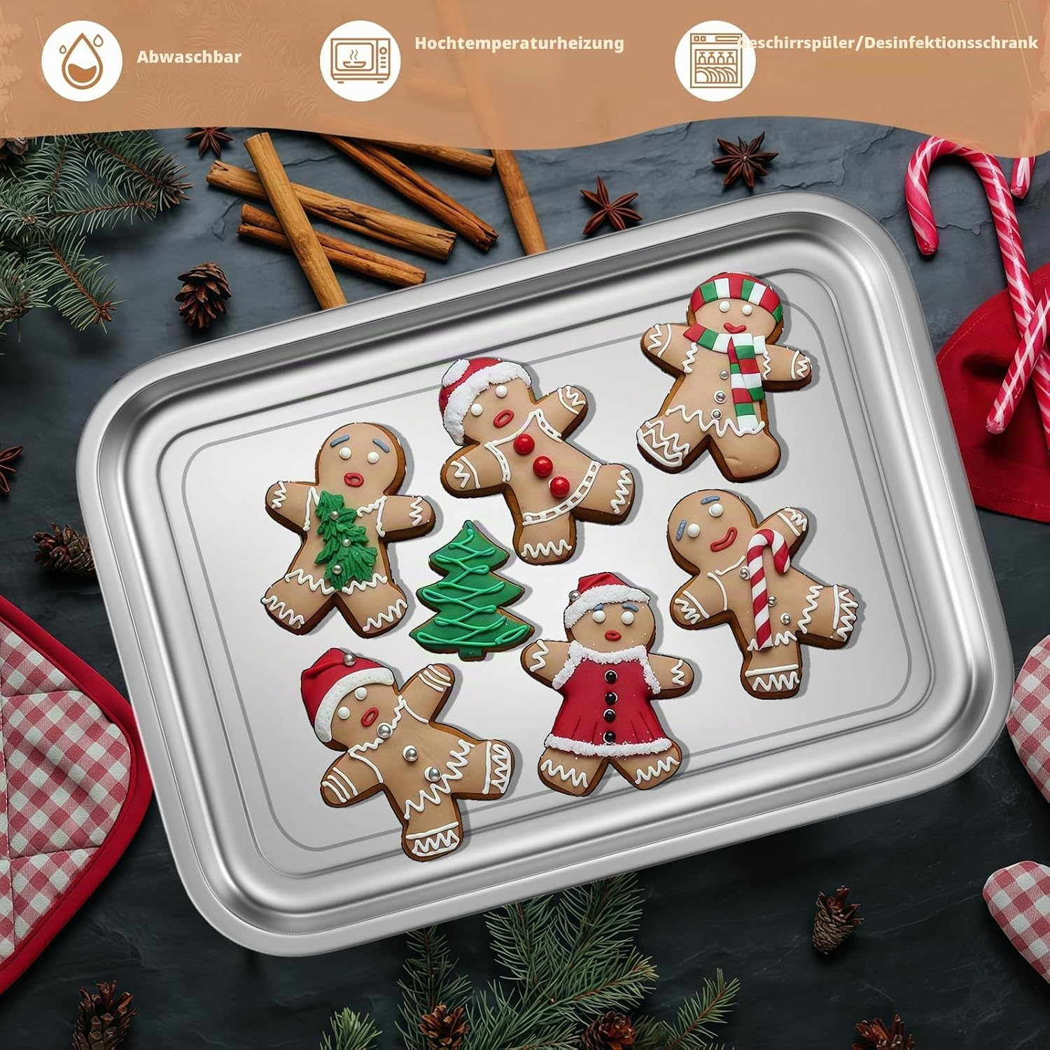 Verschiedene Weihnachtsplätzchen in Form von Lebkuchenmännchen auf einem silbernen Blech, umgeben von Tannenzweigen und Zimtstangen.