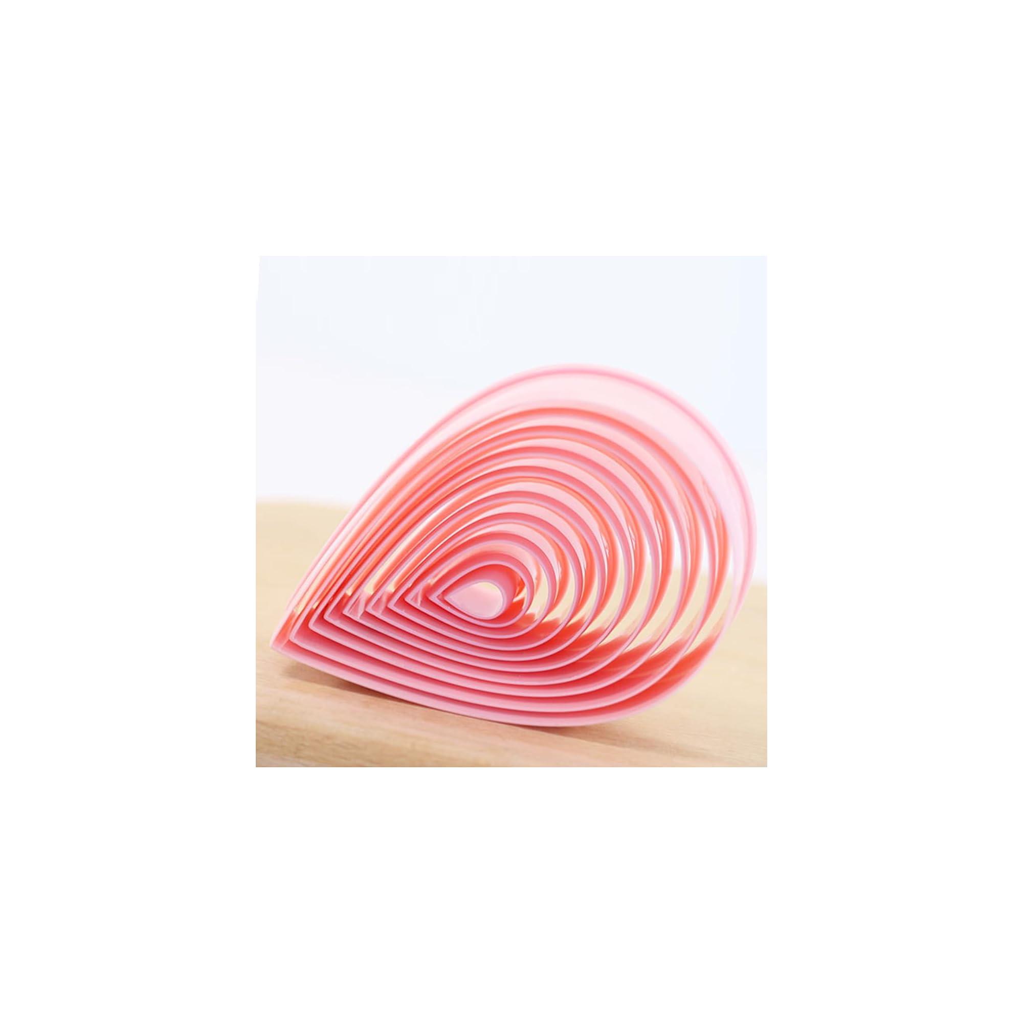 Ein Set ineinandergesteckter rosa tropfenförmiger Plastikausstecher auf Holz vor weißem Hintergrund.
