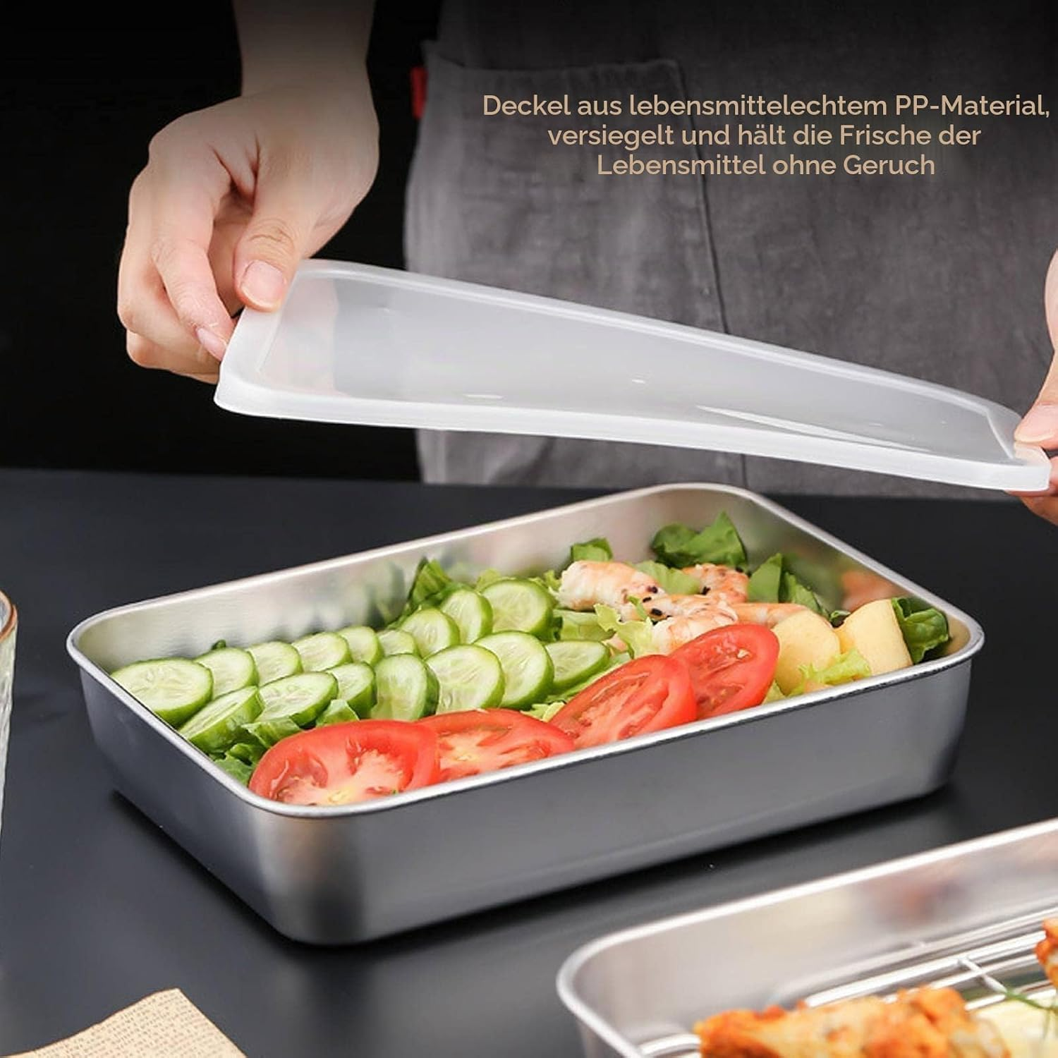 Eine Person öffnet den Deckel einer Edelstahl-Frischhaltebox mit Salat, Tomaten und Gurken.